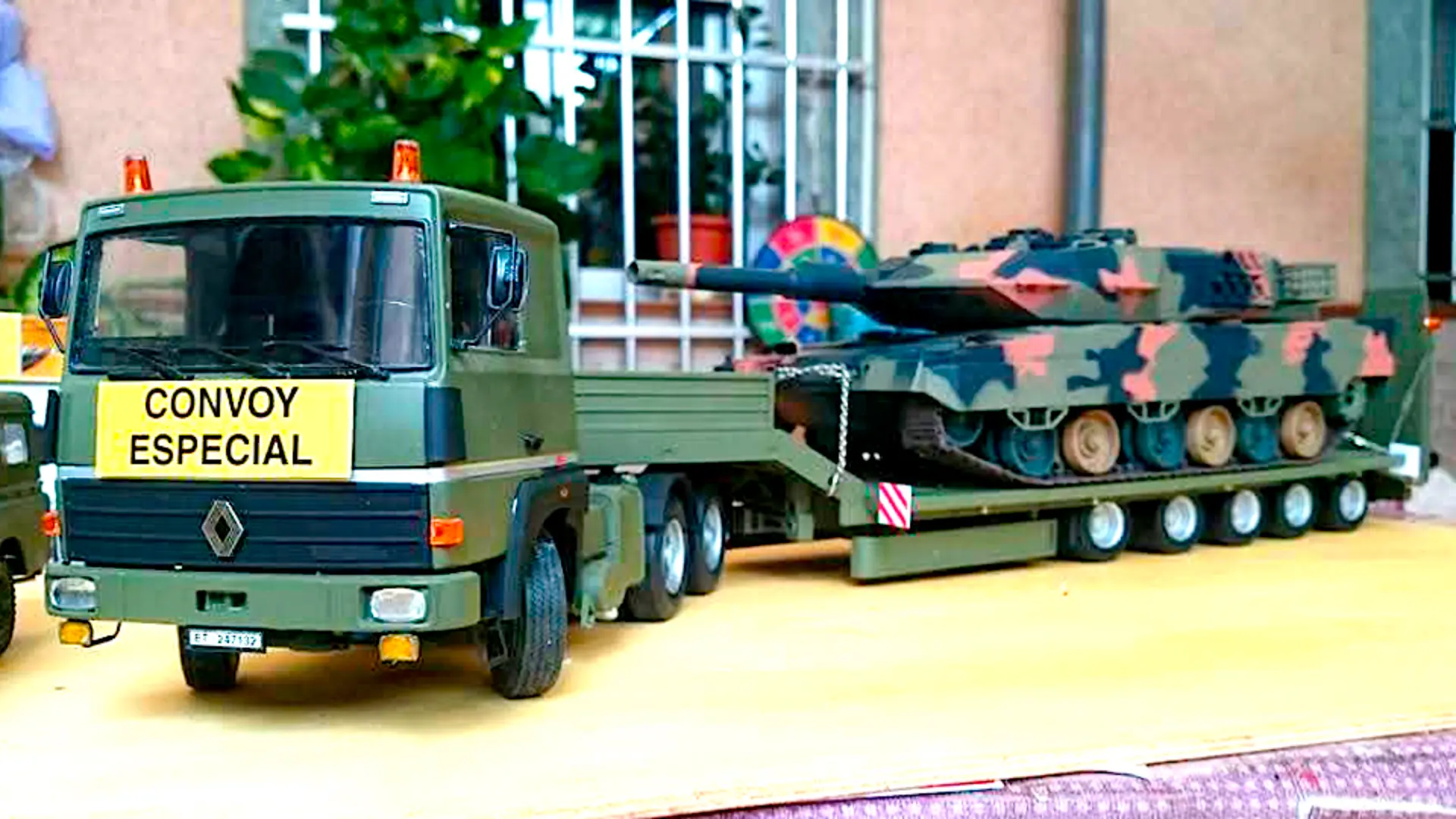 Un camión verde a escala 1:24 con el cartel "CONVOY ESPECIAL" transporta un tanque camuflado en un remolque, perfecto para los entusiastas de las maquetas de camiones y la colección de cualquier camionero.