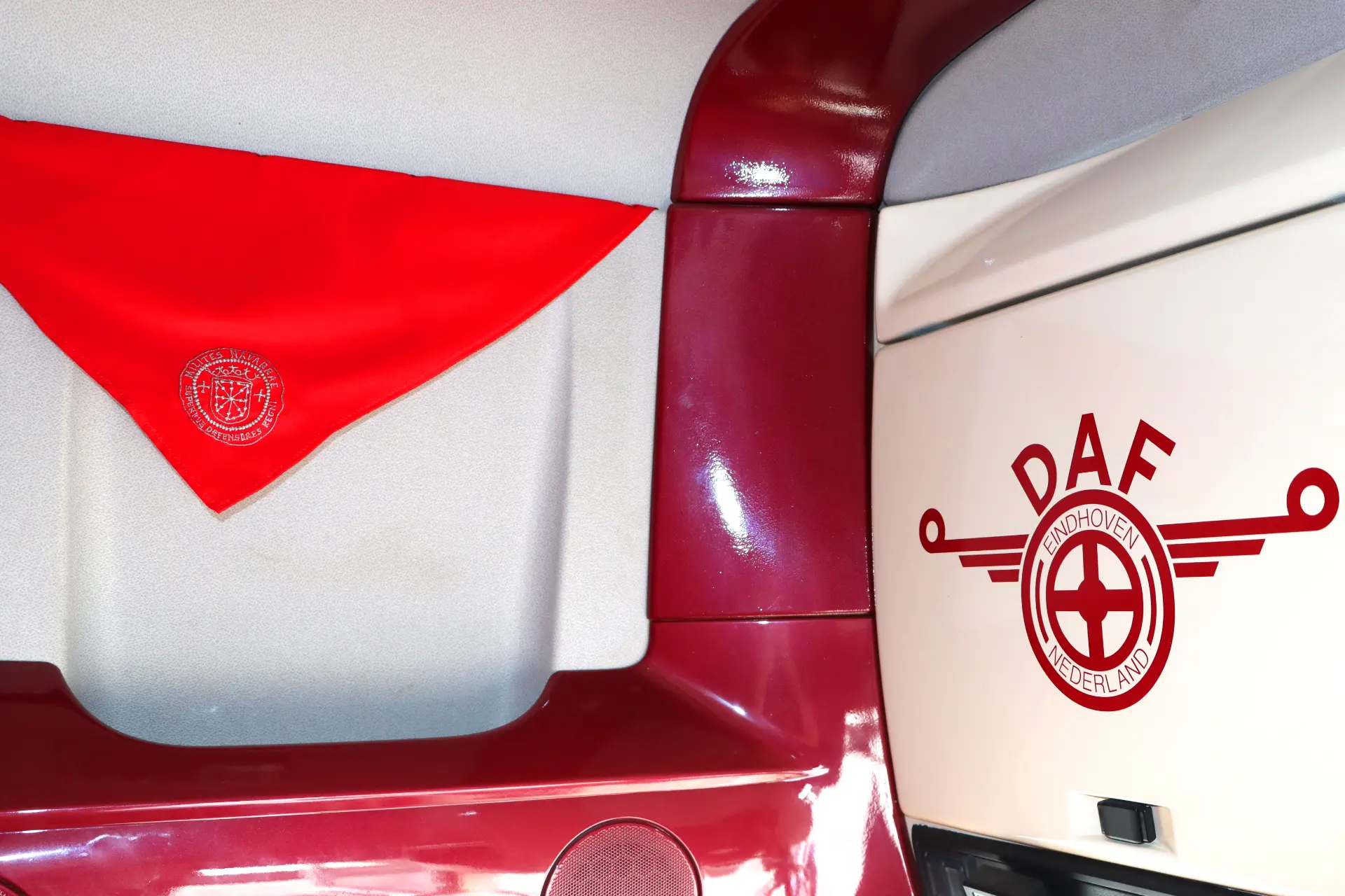 Interior de camión DAF rojo, con una tela roja y el logotipo de DAF Eindhoven Países Bajos sobre una superficie blanca.
