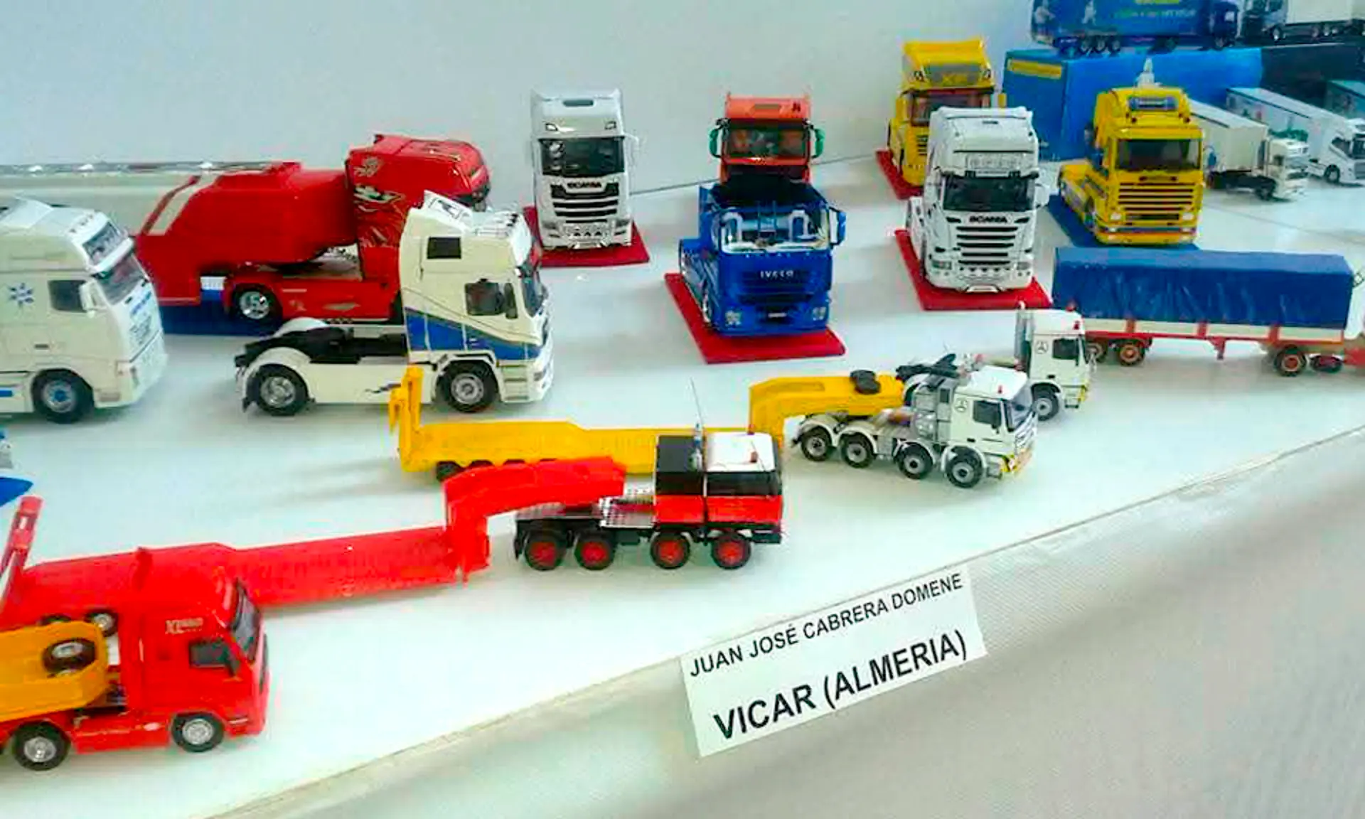 Maquetas coloridas de camiones y remolques a escala 1:24 se muestran sobre una mesa, con una etiqueta que dice "Vicar (Almería)".