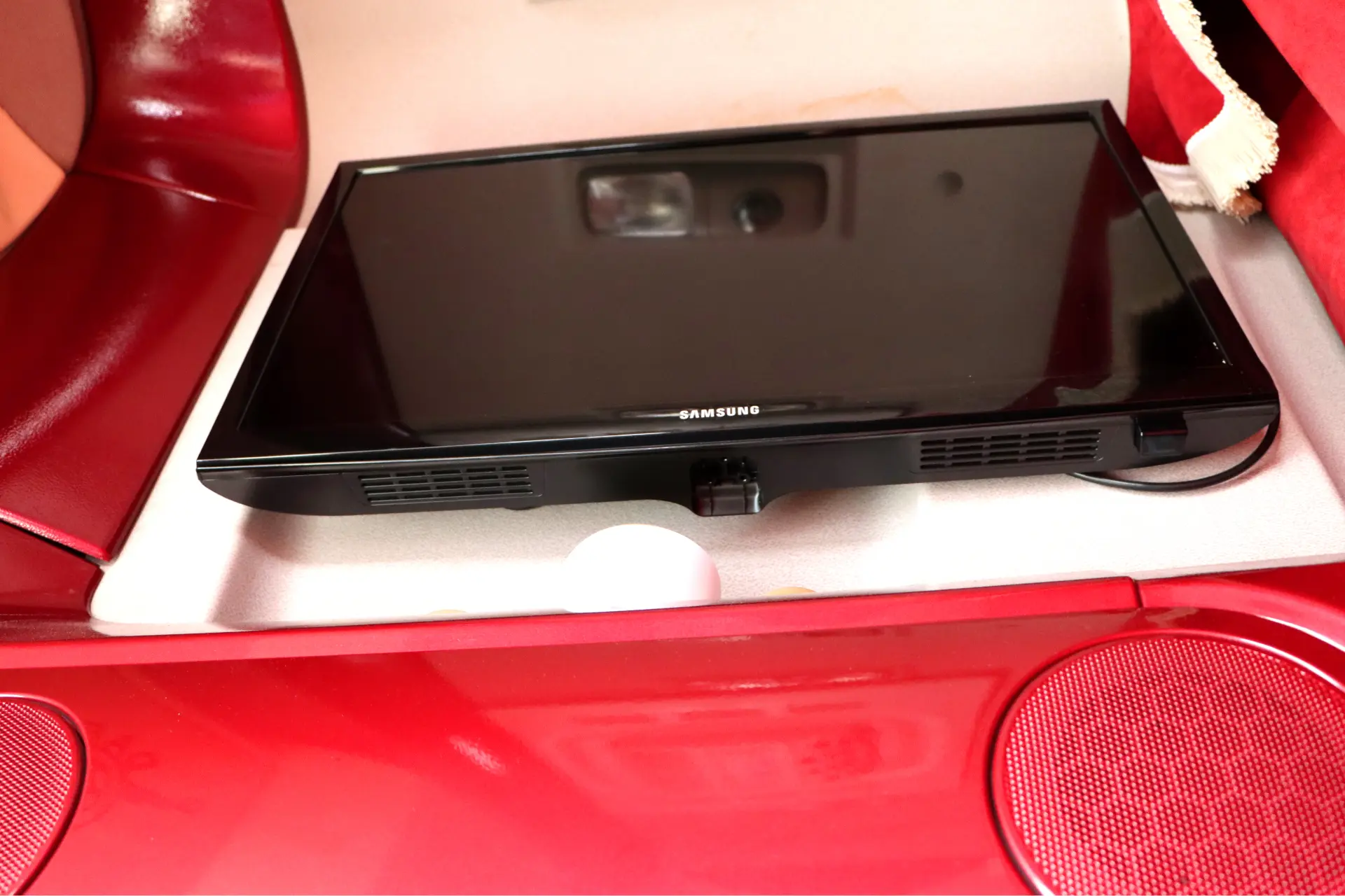 Un monitor Samsung negro colocado sobre una superficie blanca, rodeado de objetos rojos y blancos.