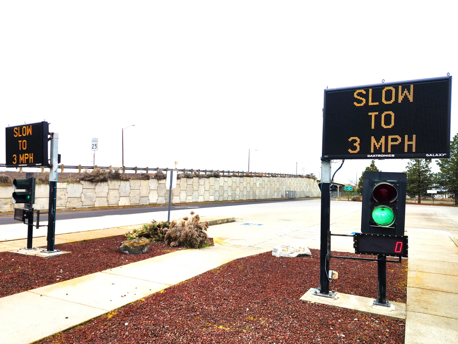 Dos señales electrónicas y un semáforo en verde indican a los conductores que reduzcan la velocidad a 3 mph en un área de estacionamiento, a menudo utilizados para inspecciones en la carretera o controles de camiones para garantizar la seguridad y el cumplimiento.