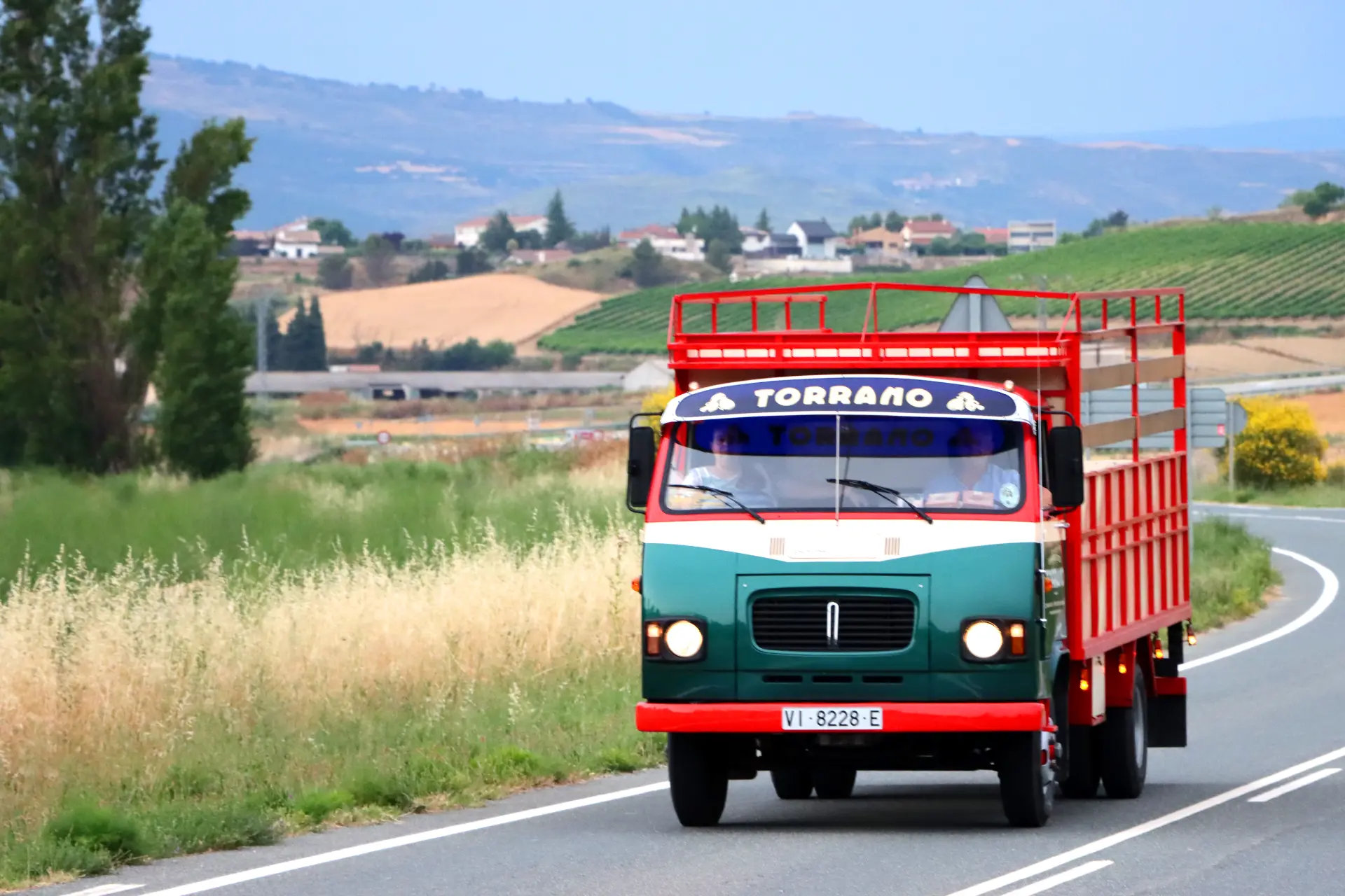 Un Avia 5000 clásico circula por una carretera rural con campos y colinas al fondo, evocando recuerdos de un camión clásico familiar de los días de Carlos Torrano.