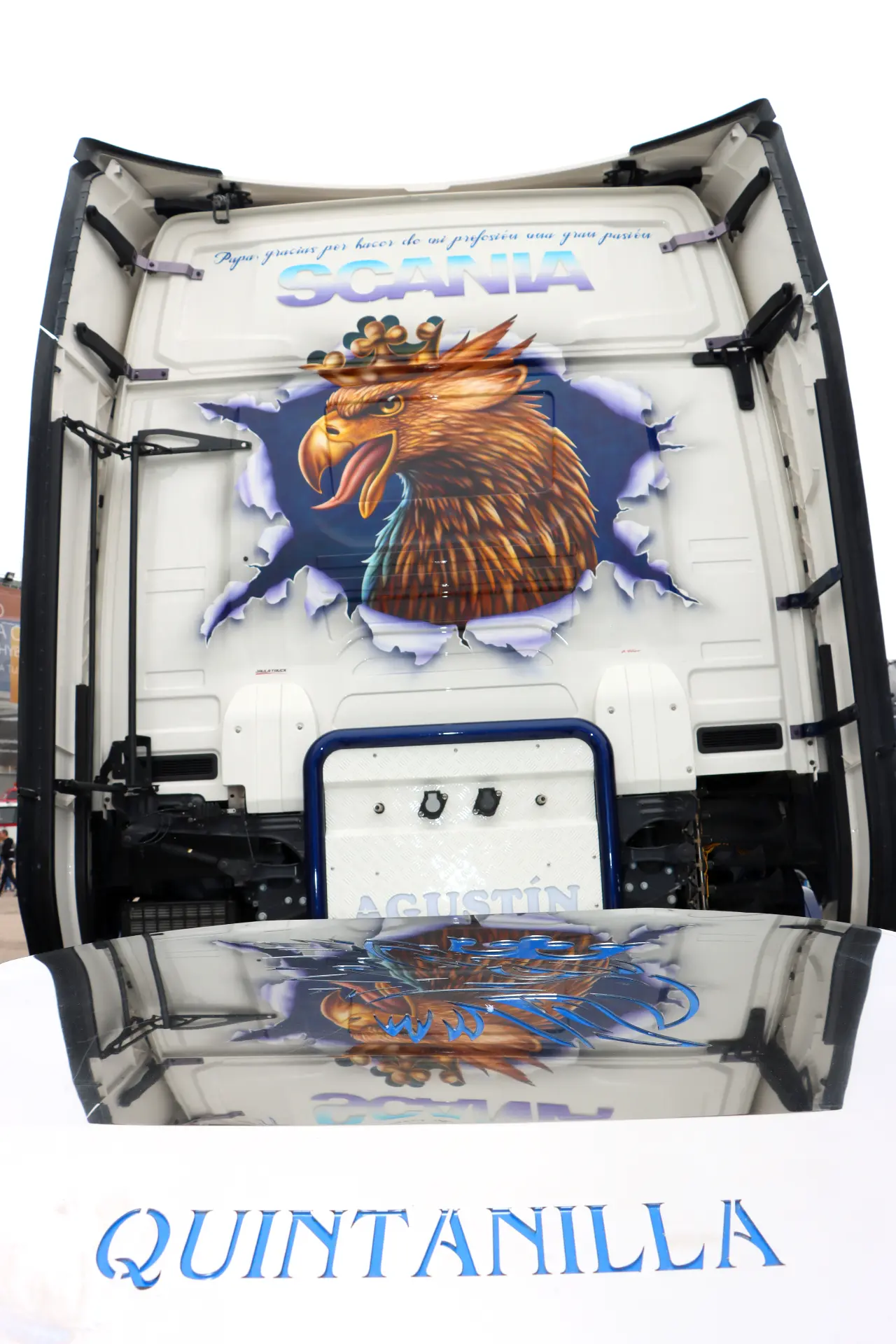La cabina de un camión exhibe un águila pintada con una corona y "QUINTANILLA" sobre una superficie reflectante, encarnando el espíritu de los camiones americanos tuneados que se ven en las carreras de camiones España y eventos como el Valencia Nascar Fest 2025.