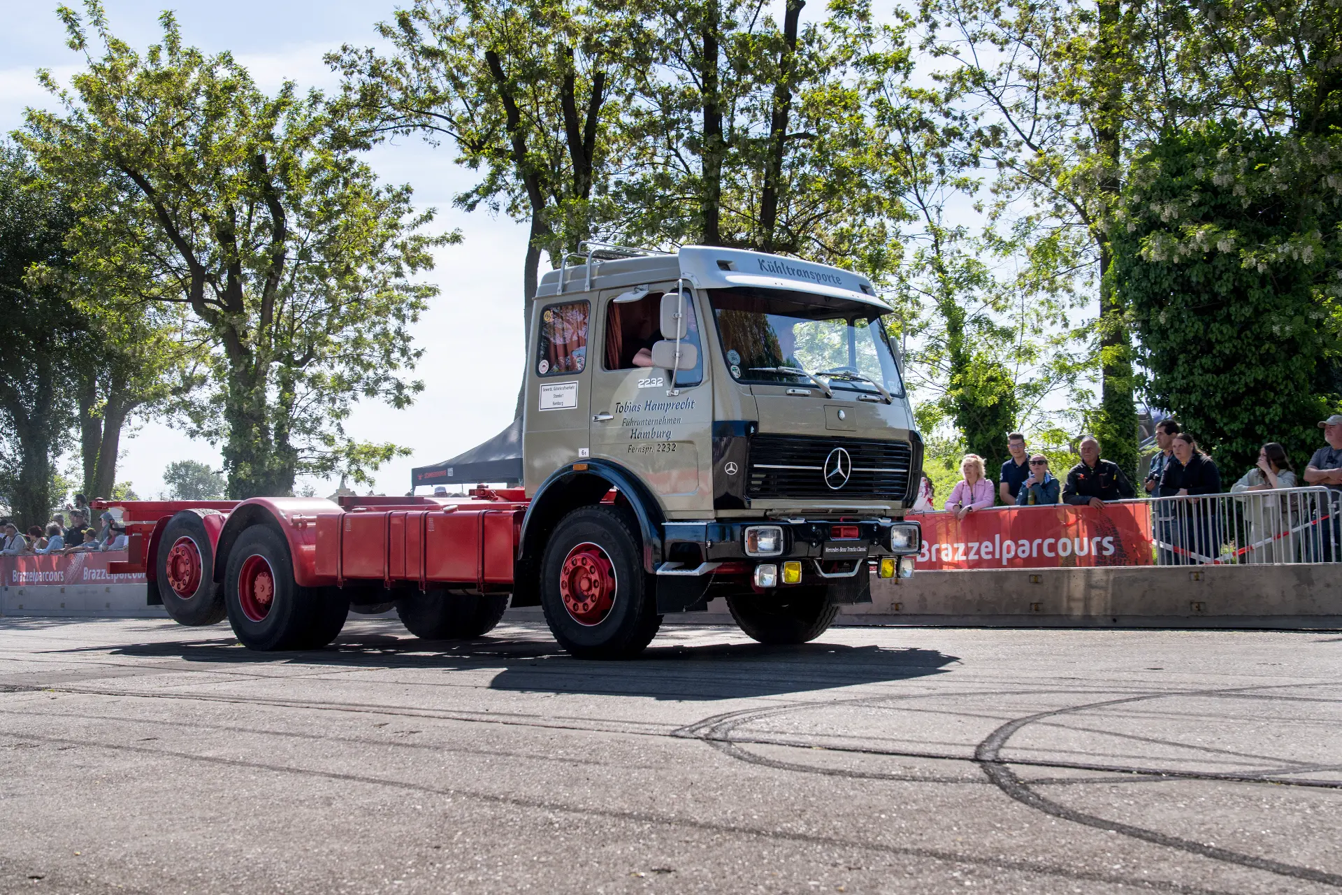 Un camión clásico Mercedes-Benz con chasis rojo se exhibe al aire libre ante una multitud en un día soleado, con un diseño clásico y el toque distintivo del Borrador automático.