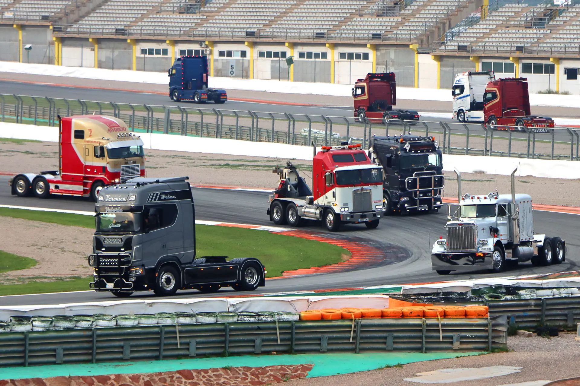 Varios grandes camiones americanos tuneados circulan por una pista de carreras con tribunas vacías al fondo en el Valencia Nascar Fest 2025, mostrando la emoción de las carreras de camiones España.