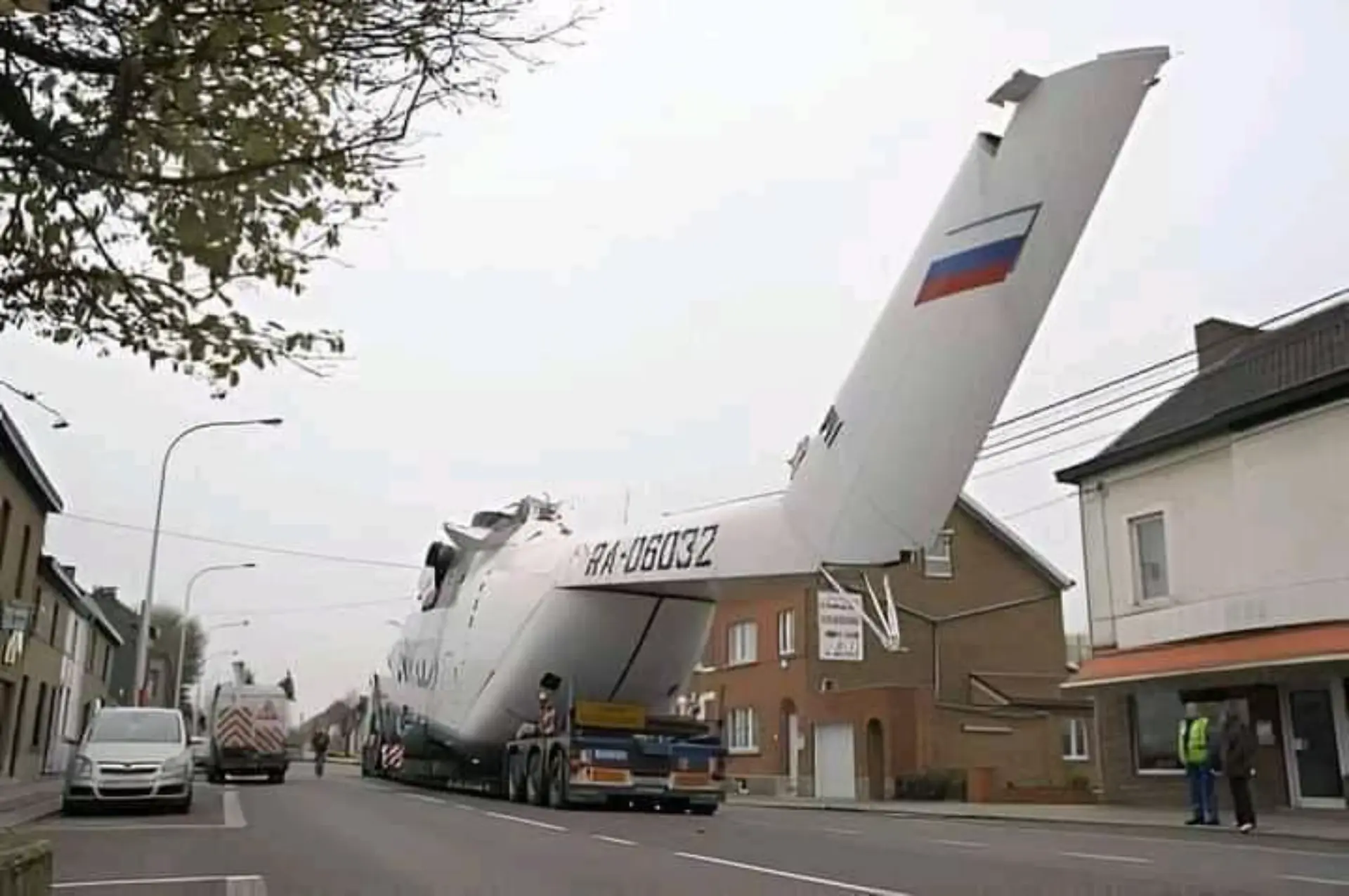 Una gran sección de cola de avión con una bandera rusa es transportada en camión a través de una calle residencial.