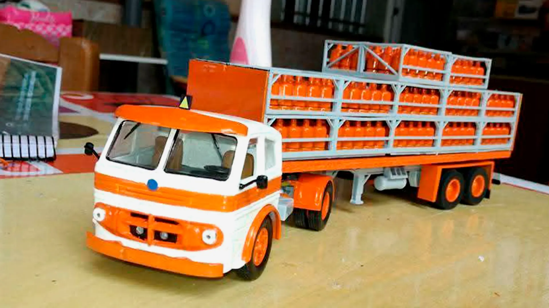 Maqueta de camión que transporta cilindros de gas de color naranja apilados en su remolque, exhibida sobre una mesa en el interior: un ejemplo impresionante de las maquetas de camiones creadas por el camionero Juan José Cabrera.