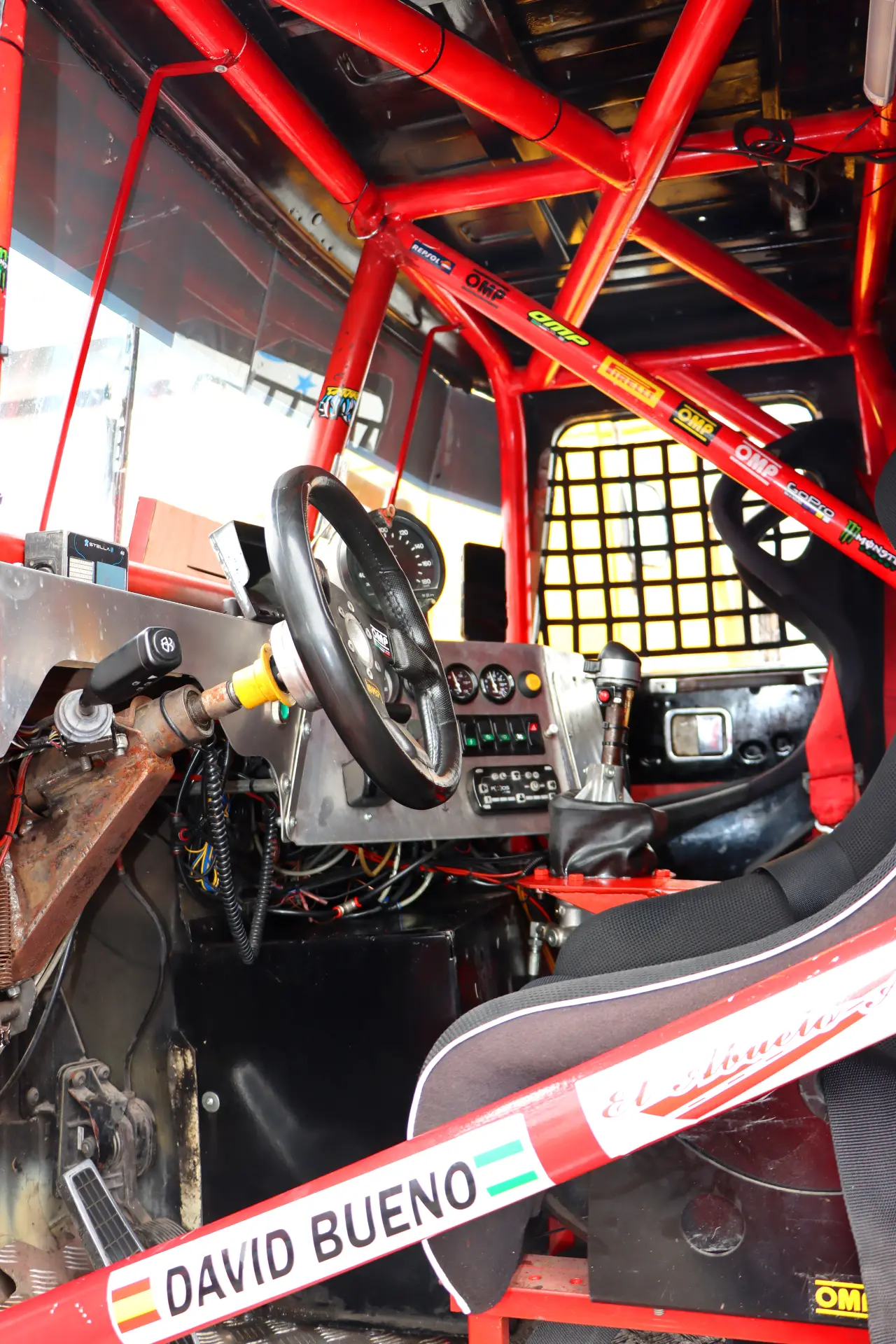 Interior de un coche de carreras todoterreno rojo, que muestra el volante, el tablero y las barras de seguridad, perfecto para los fanáticos de las carreras de camiones España o aquellos que esperan con ansias el Valencia NASCAR Fest 2025.