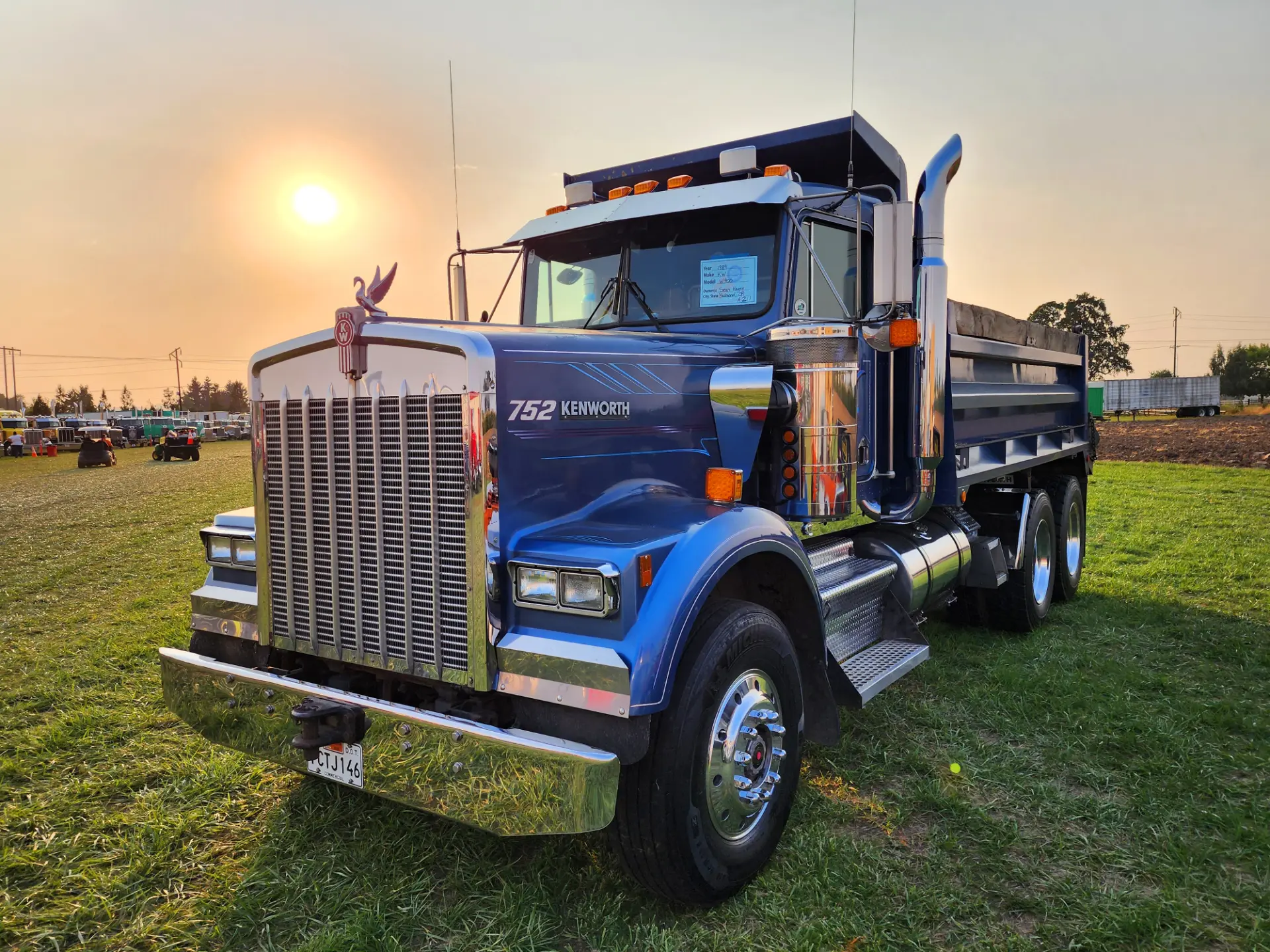 Camión volquete Kenworth azul estacionado en el césped al atardecer, con detalles cromados que reflejan la luz del sol, listo para las inspecciones en EE.UU. para garantizar el cumplimiento y evitar sanciones en carretera.