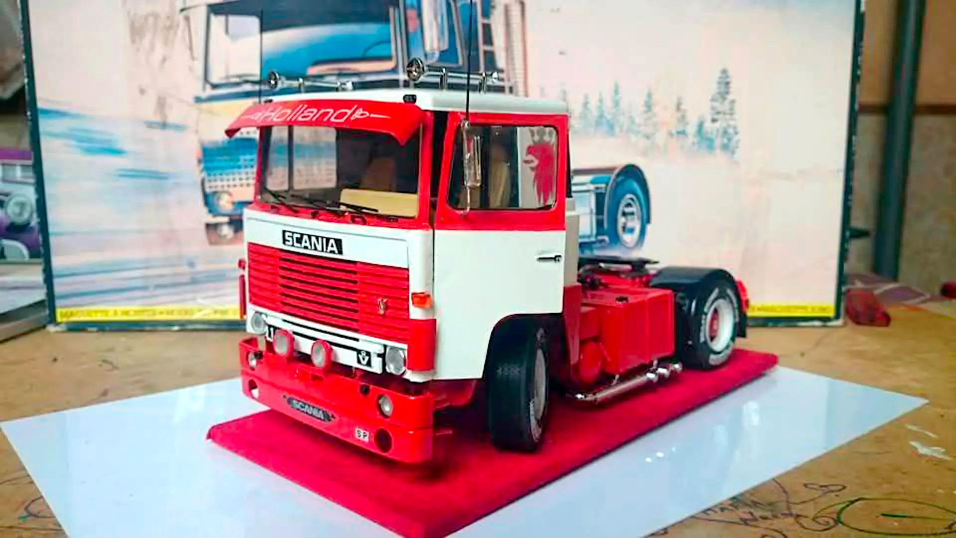 Un modelo detallado de camión Scania exhibido en una plataforma roja, con un póster de camión en el fondo, resalta la precisión de la tecnología del borrador automático.