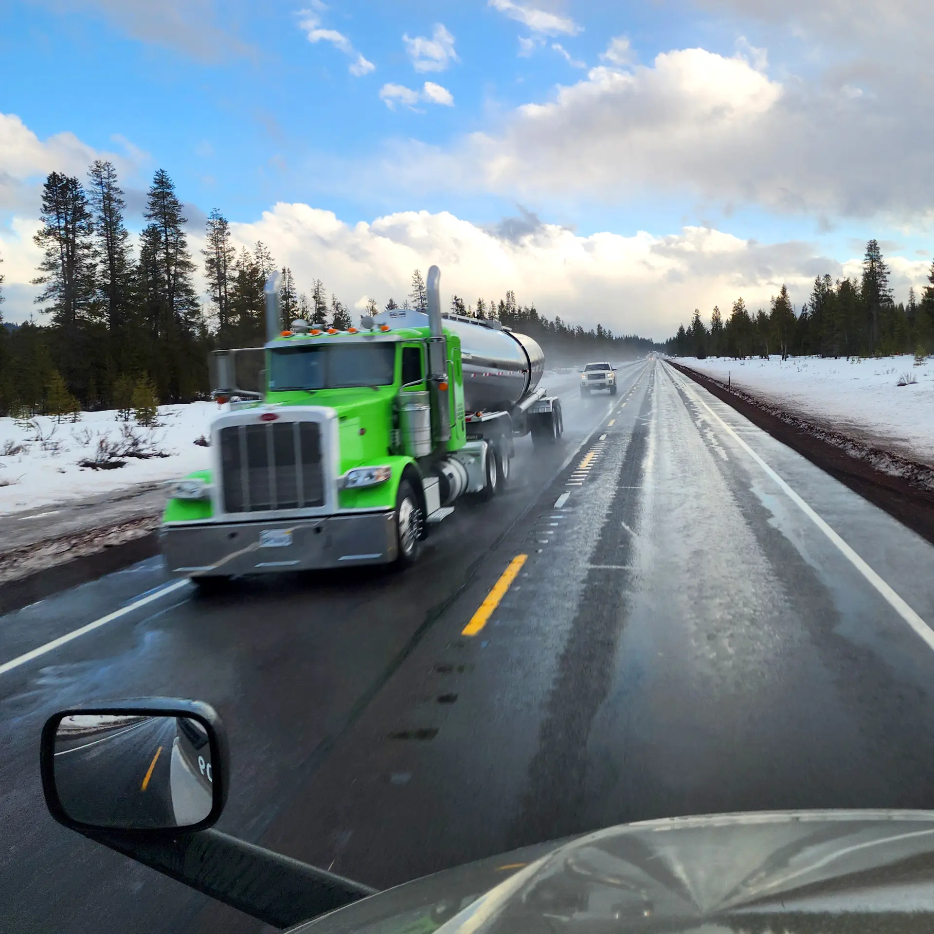 Un camión semirremolque verde circula por una carretera mojada y nevada con árboles y un cielo nublado al fondo, lo que resalta la importancia de controlar un camión incluso en condiciones climáticas difíciles.