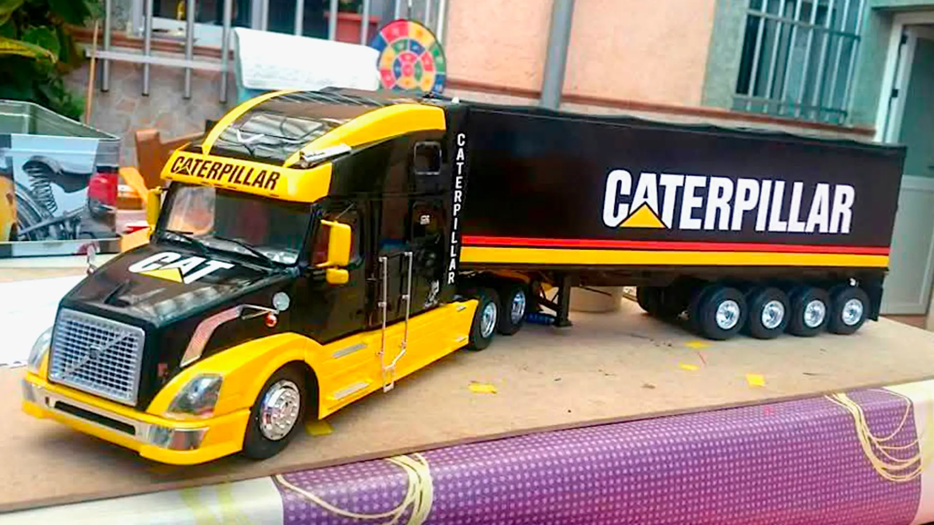 Un modelo detallado de camión y remolque con la marca "Caterpillar" en colores negro, amarillo y naranja, perfecto para coleccionistas o como pieza de exhibición.