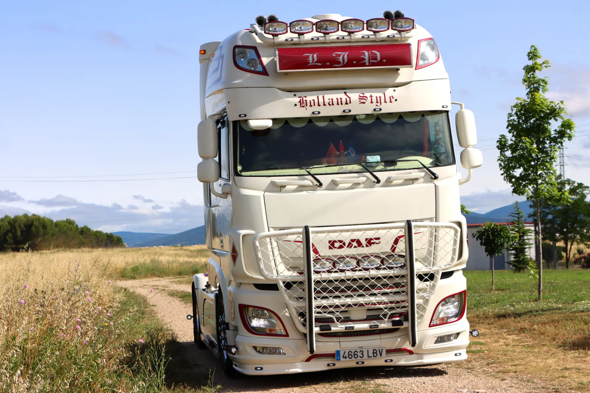 Un gran camión DAF blanco con "Holland Style" en el frente está estacionado en un camino de tierra rural.