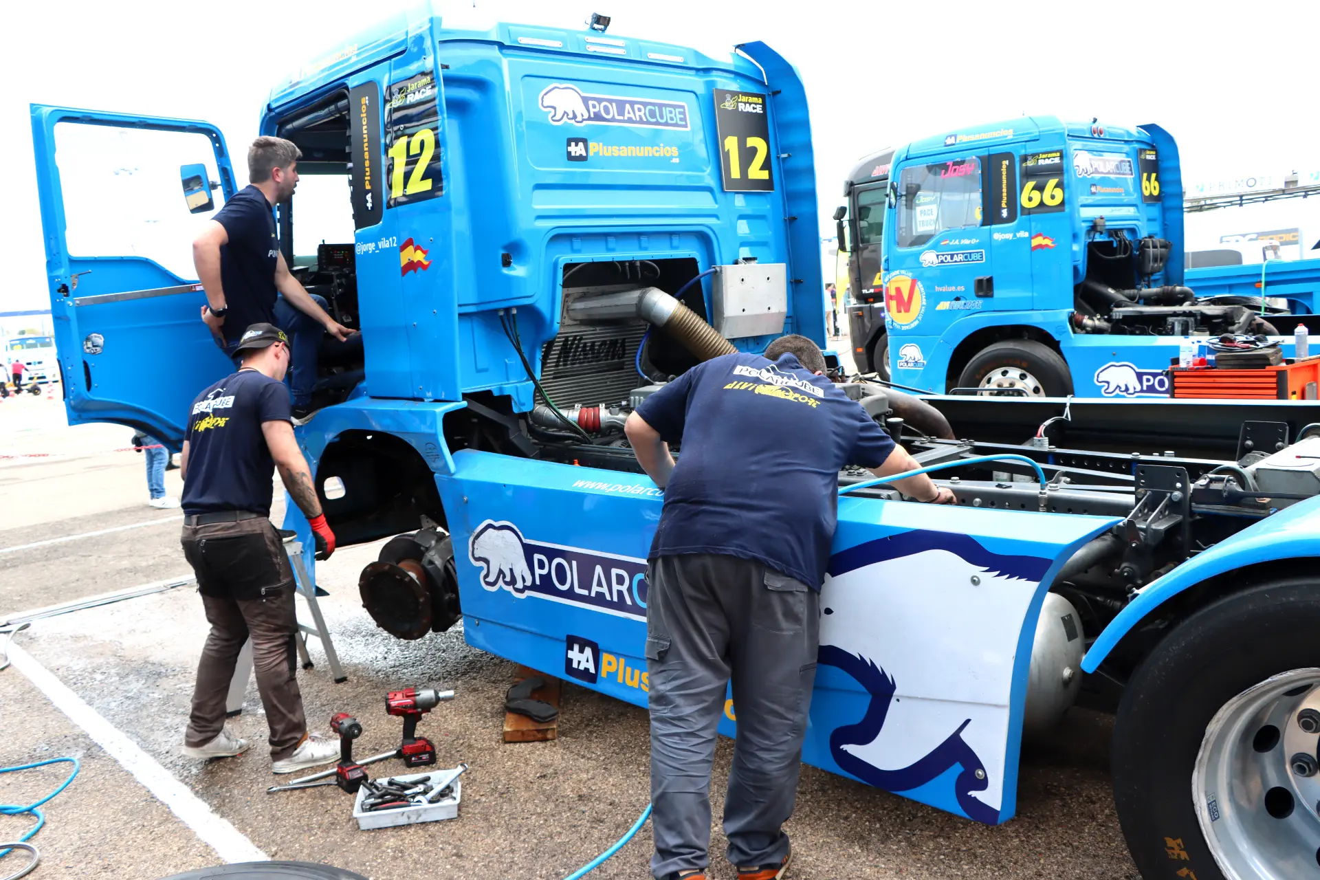 Tres mecánicos trabajan en un camión de carreras Polarbruse azul con su motor expuesto en una parada en boxes, mostrando la emoción de los camiones americanos tuneados en el Valencia Nascar Fest 2025.
