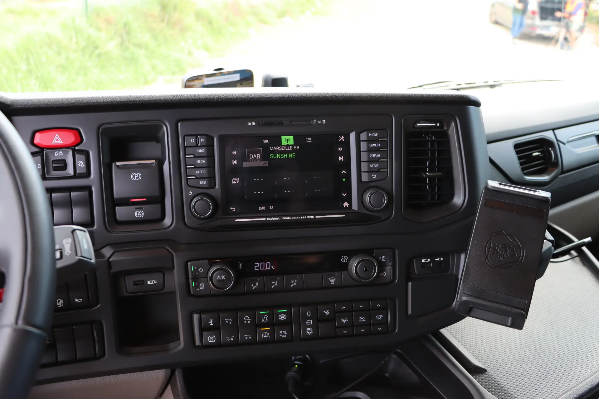 Tablero de un vehículo que muestra una pantalla de radio, salidas de aire, controles y un soporte para teléfono durante una prueba en ciudad del Scania 40R eléctrico.
