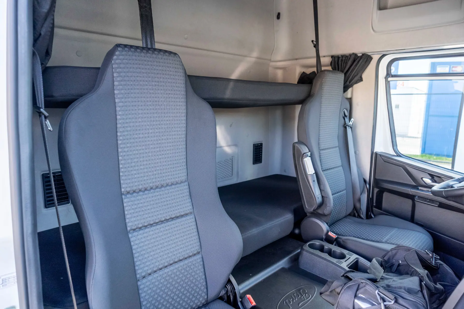 Interior de la cabina de un camión que muestra dos asientos y una litera para dormir detrás de ellos, ideal para realizar una prueba de camión Ford o compartir tu opinión sobre un tractor Ford mientras disfrutas de las ventajas del cambio de 16 velocidades.