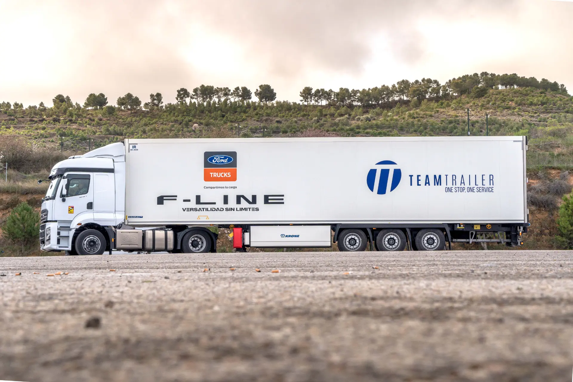 Remolque del equipo blanco F-Line, camión estacionado en un camino de tierra, mostrando el poder de los camiones Ford F-Line 1845T, con árboles y un cielo nublado en el fondo.