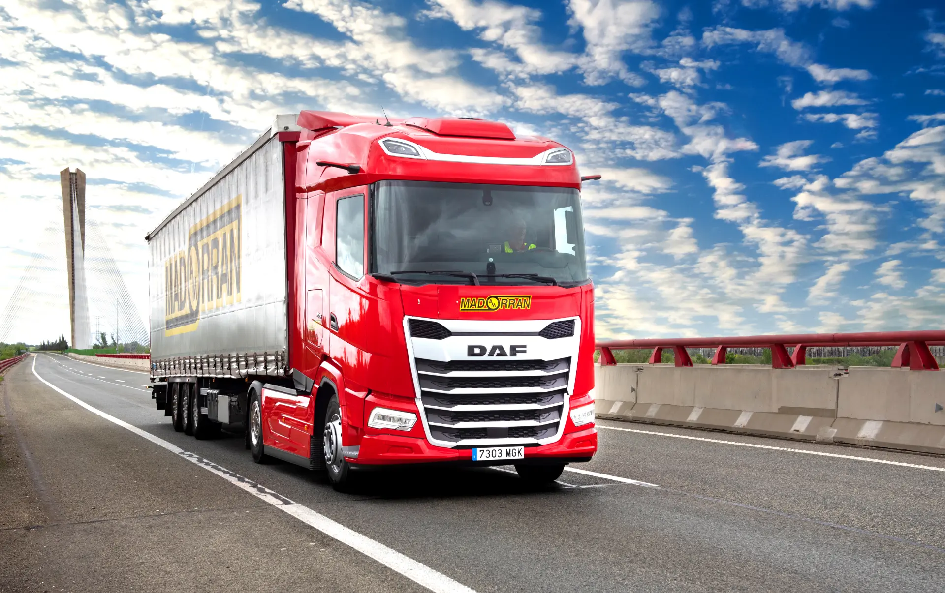 Un camión semirremolque DAF de color rojo brillante, con tecnología Borrador automático, circula por una autopista bajo un cielo azul con nubes dispersas.