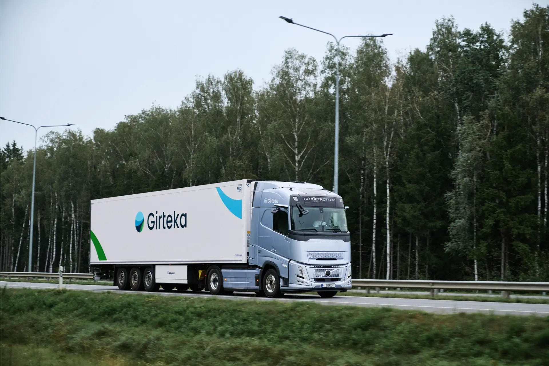 Un camión Volvo FH de la marca Girteka, conocido por su comodidad, transporte y eficiencia, circula por una autopista junto a una zona boscosa.