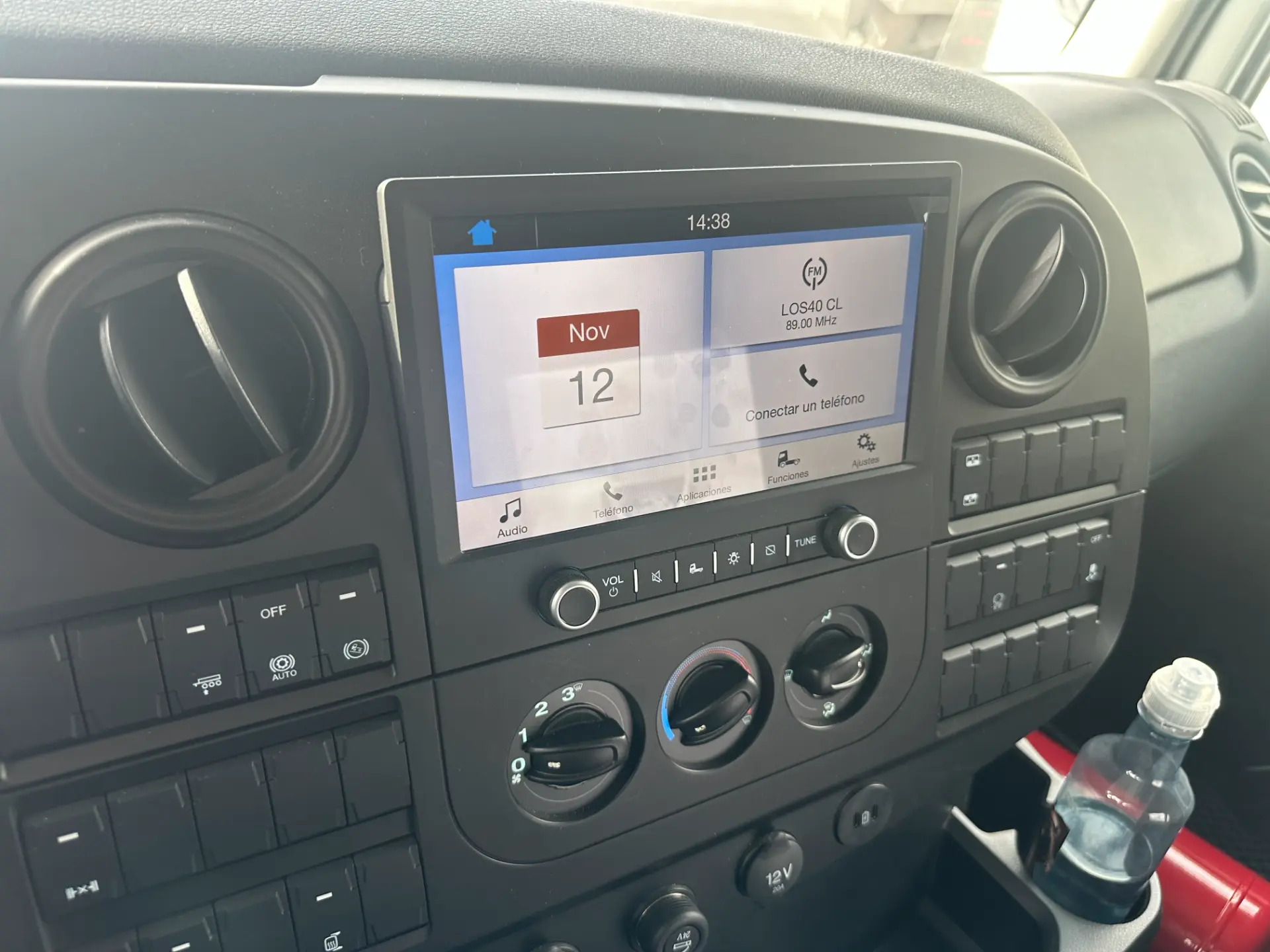 Tablero de automóvil con pantalla táctil que muestra la fecha 12 de noviembre y varios controles, botella de agua cerca, ideal para quienes consideran el consumo Ford L-Line o buscan ventajas del cambio de 16 velocidades.