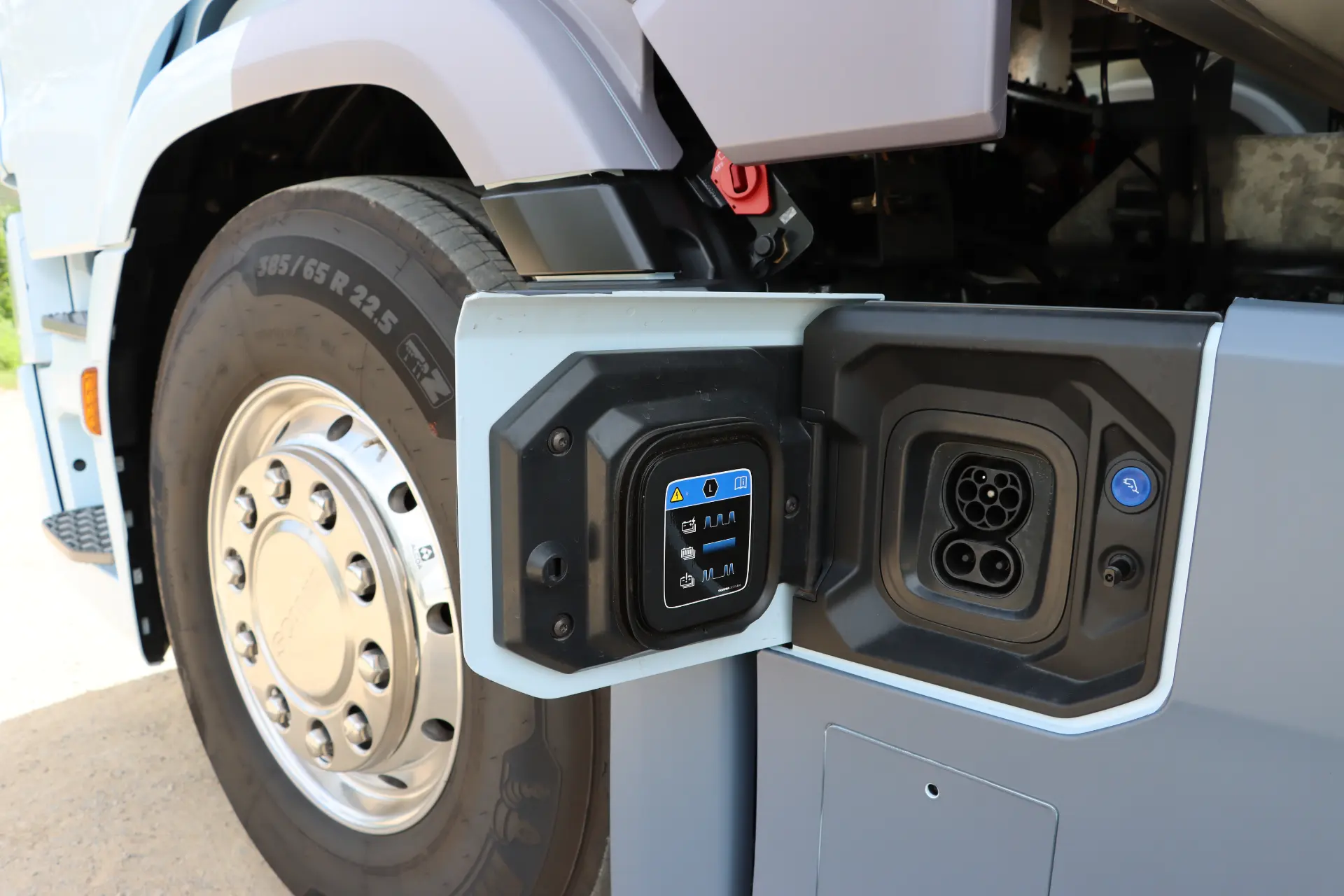 Primer plano del puerto de carga y panel de control de un camión eléctrico Scania 40R cerca de la rueda delantera, ideal para prueba en ciudad y carretera.