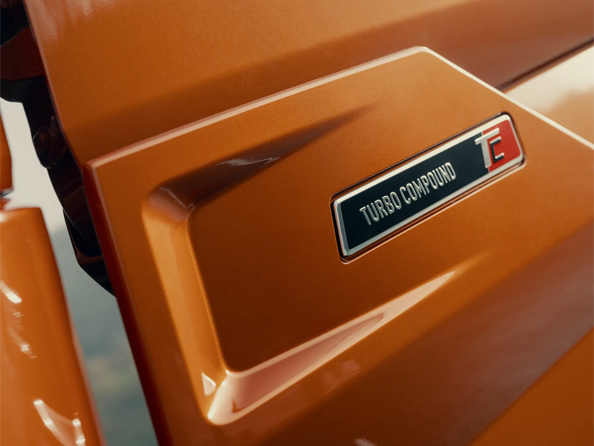 Primer plano de un vehículo naranja con una insignia "Turbo Compound" y "TC" en su costado, que presenta el sistema Borrador automático para un mejor rendimiento.