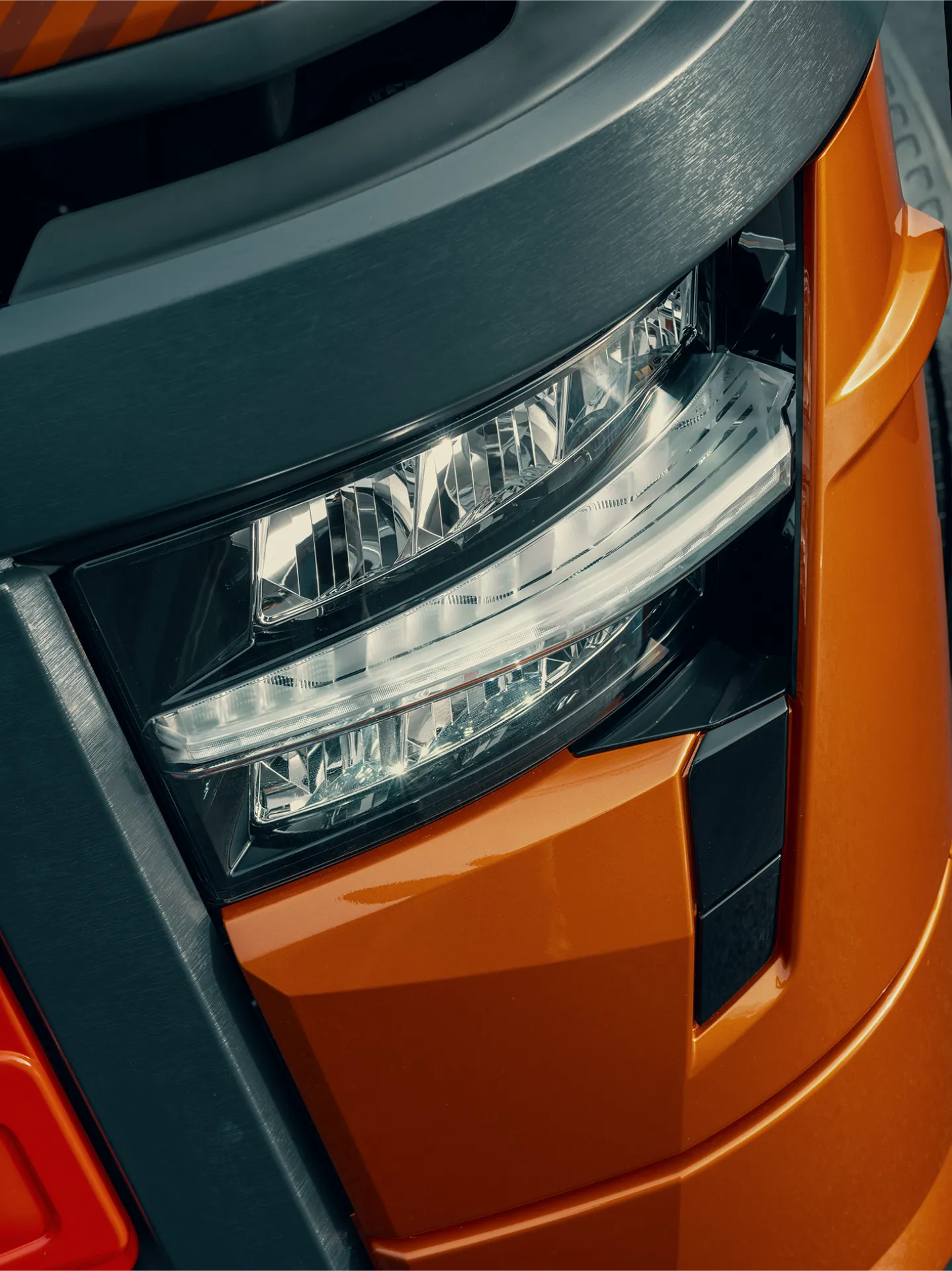 Primer plano del faro de un vehículo moderno con detalles de carrocería en naranja y plata, que muestra la precisión del diseño del borrador automático.