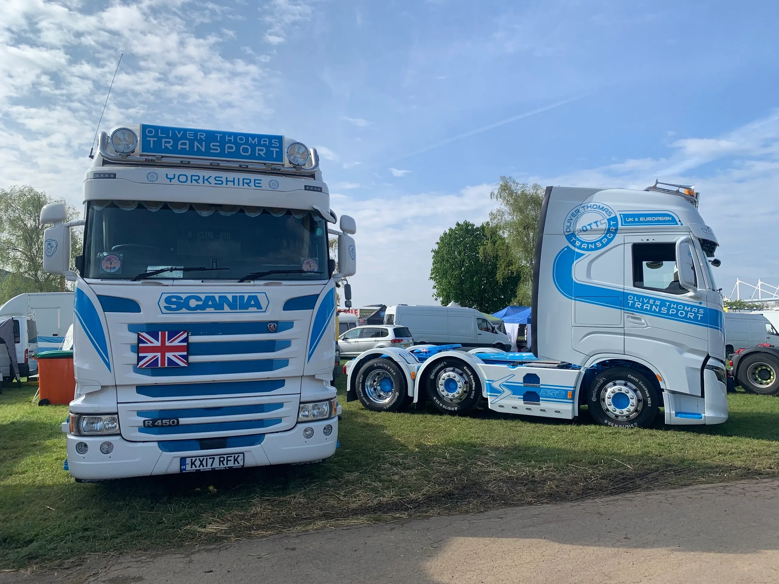 Dos camiones Scania blancos y azules con la marca "Oliver Thomas Transport" estacionados en el césped.
