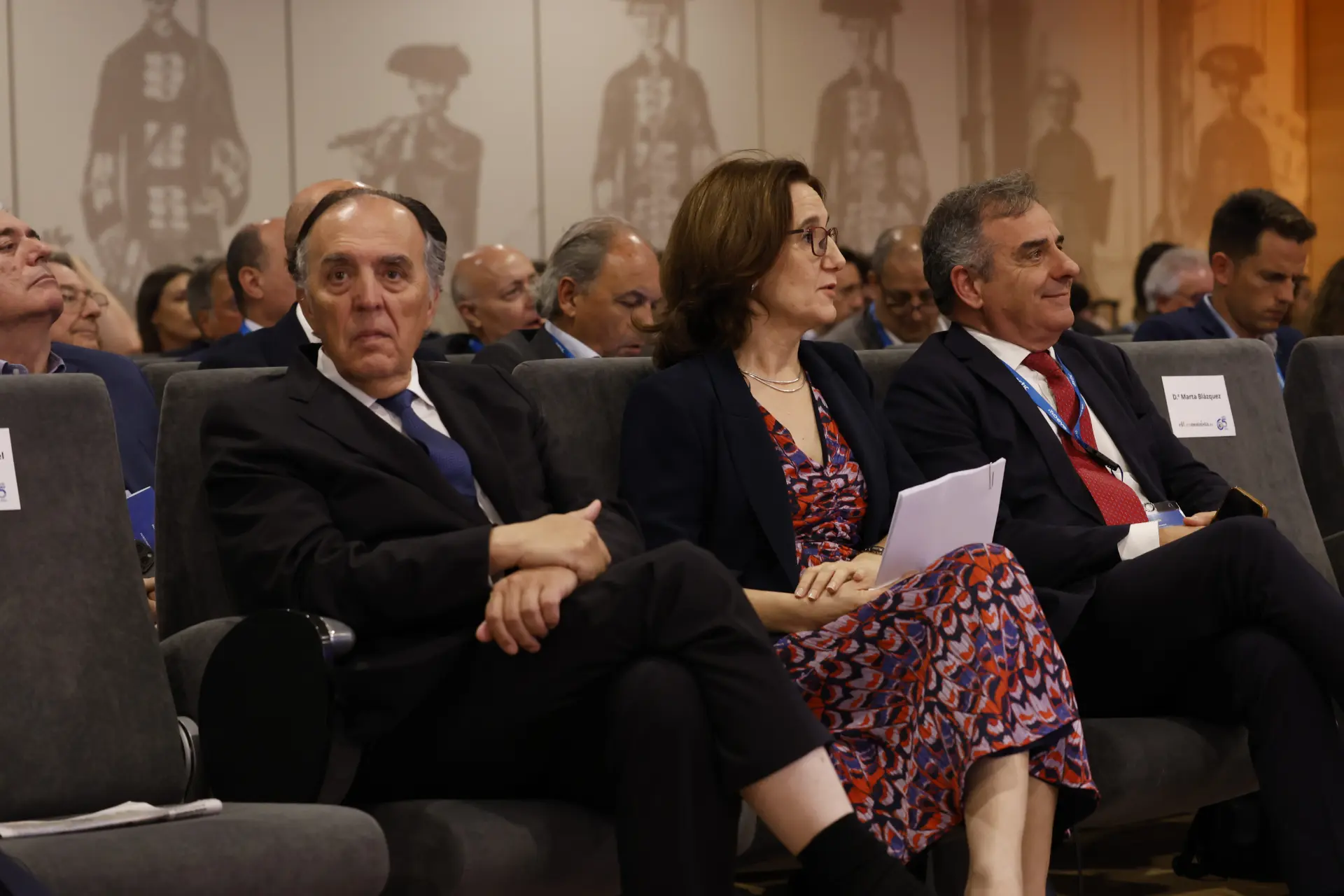 Tres personas vestidas de negocios se sientan entre el público en un evento formal, escuchando atentamente una discusión sobre transporte sostenible, camiones e innovaciones de astic transporte.