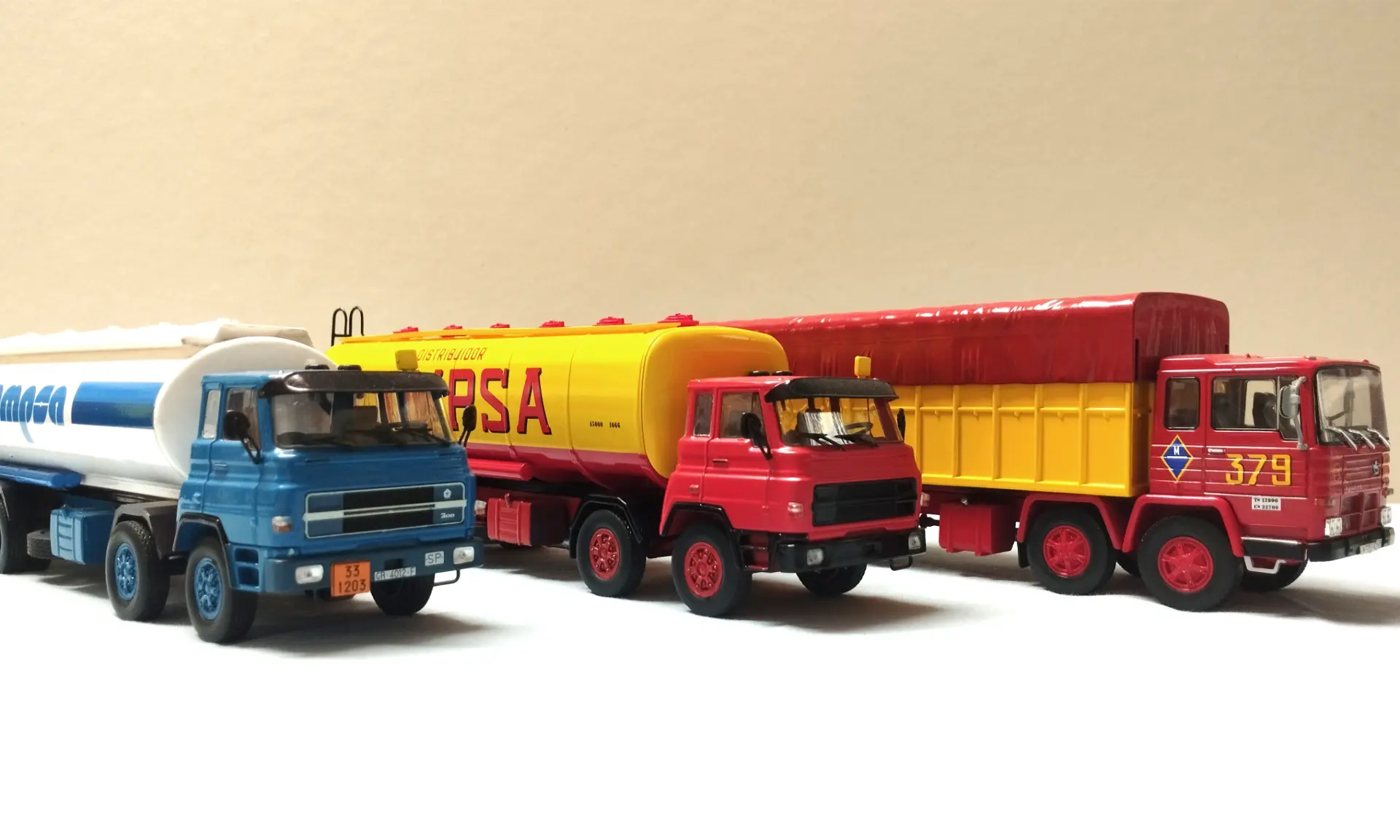 Tres coloridos camiones de juguete (azul, amarillo y rojo) están alineados uno al lado del otro sobre un fondo claro, perfecto para inspirar ideas sobre cómo personalizar camiones en miniatura y explorar el modelismo de camiones.