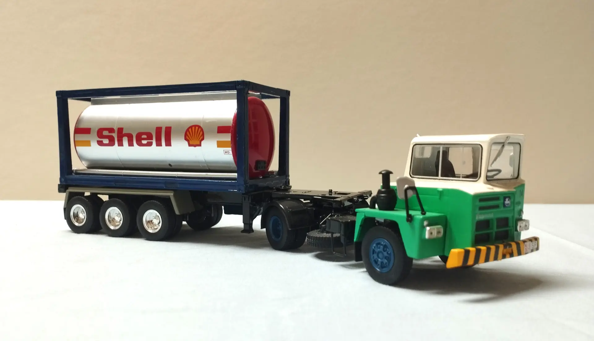 Un camión de juguete verde y blanco con un remolque cisterna de combustible de la marca Shell, perfecto para coleccionistas de camiones a escala 1:43, exhibido sobre un fondo claro.