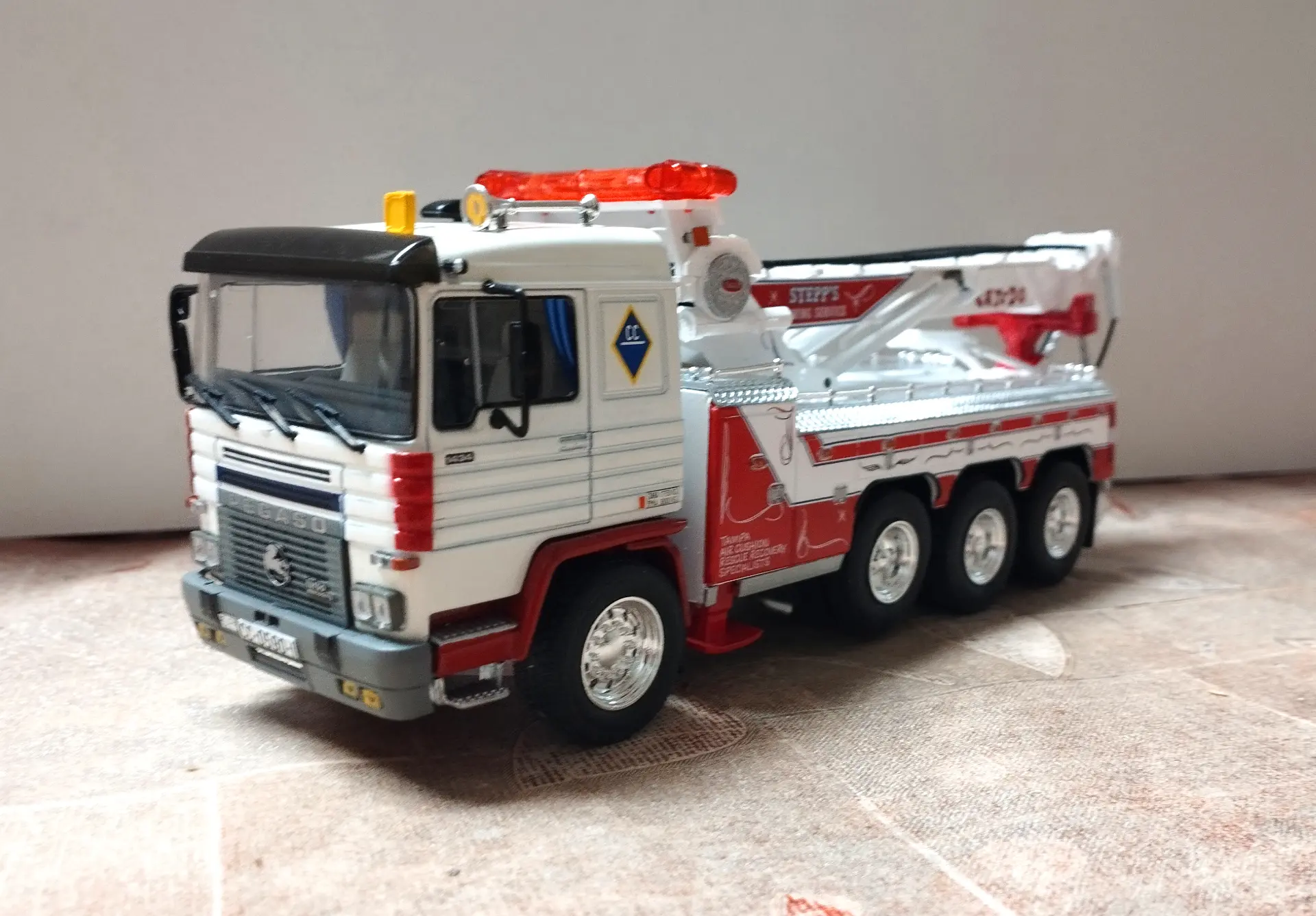 Un modelo de grúa blanca y roja de cuatro ejes, perfecto para coleccionistas de camiones a escala 1:43, expuesto sobre una superficie de color claro.