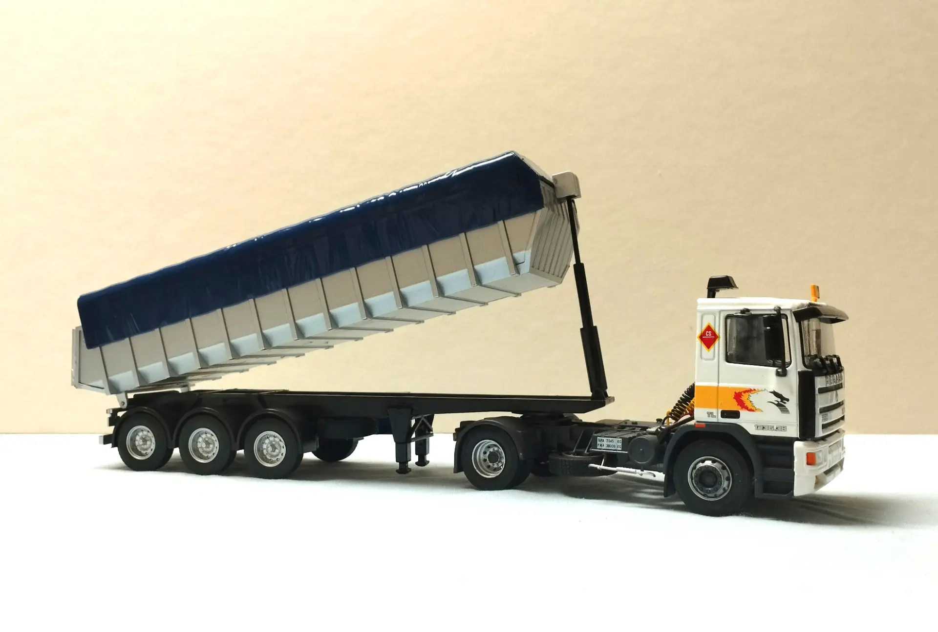 Un camión volquete blanco con un remolque elevado azul y plateado, que se muestra sobre un fondo liso, perfecto para coleccionistas de maquetas de camiones o aquellos que buscan camiones detallados a escala 1:43.