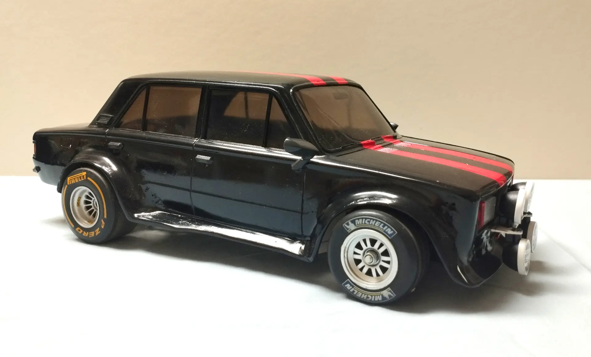 Un coche de juguete negro con franjas de carreras rojas y faros de rally expuestos, visto desde un lado, perfecto para coleccionistas de maquetas de camiones o fanáticos de los camiones a escala 1:43.