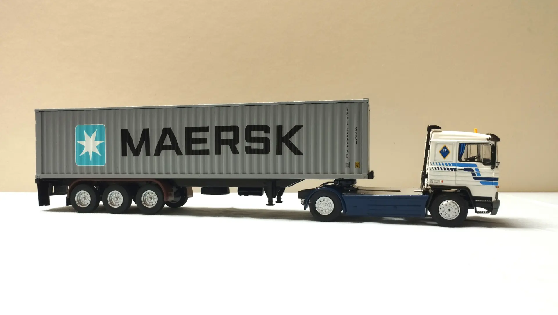 Un modelo de camión detallado con un remolque contenedor de envío MAERSK, perfecto para coleccionistas de camiones a escala 1:43 o maquetas de camiones, presentado sobre un fondo liso.