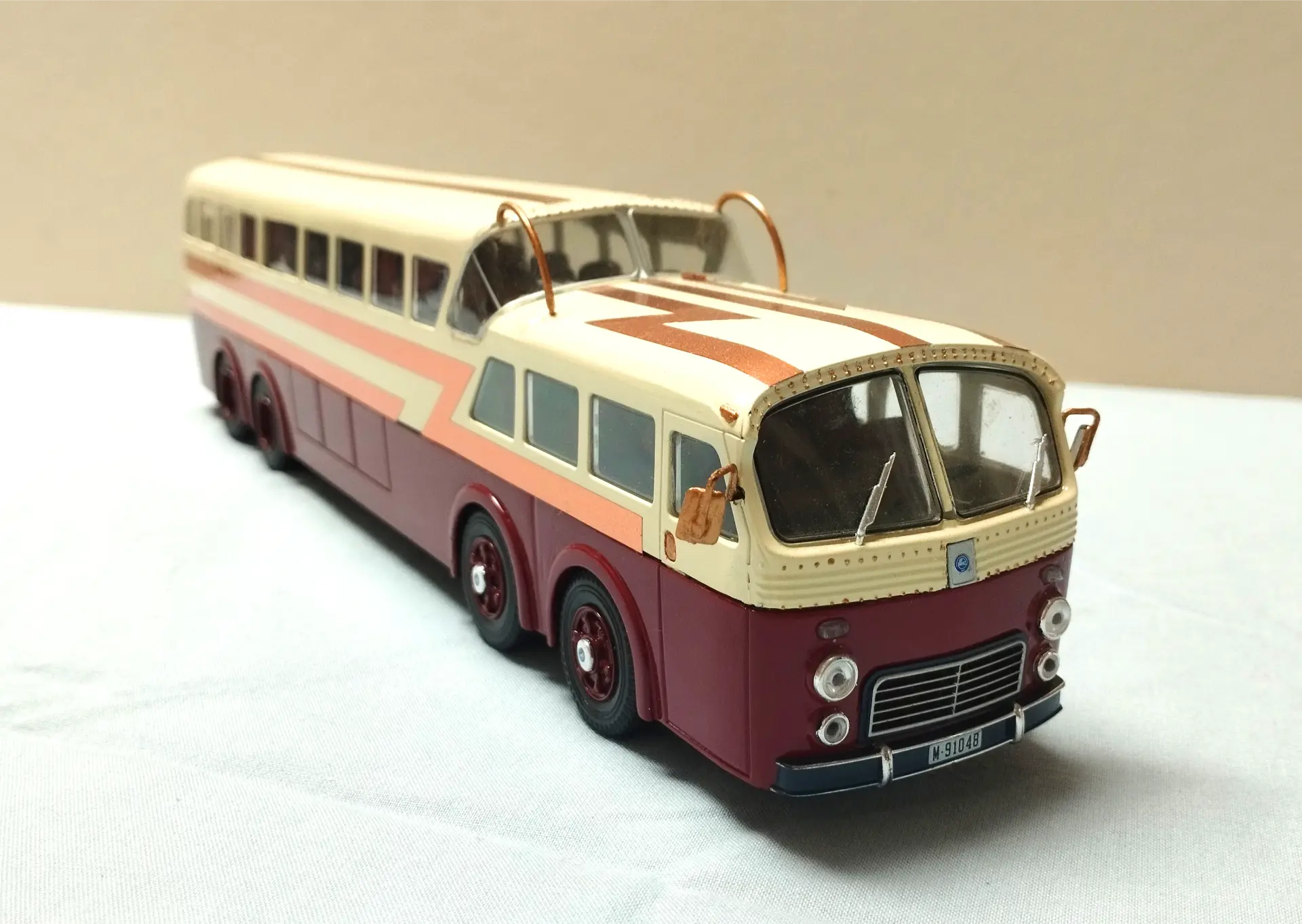 Un autobús vintage alargado con un esquema de colores crema y granate sobre una superficie clara, ideal para coleccionistas de maquetas de camiones a escala 1/43 o aquellos que buscan maquetas personalizadas.