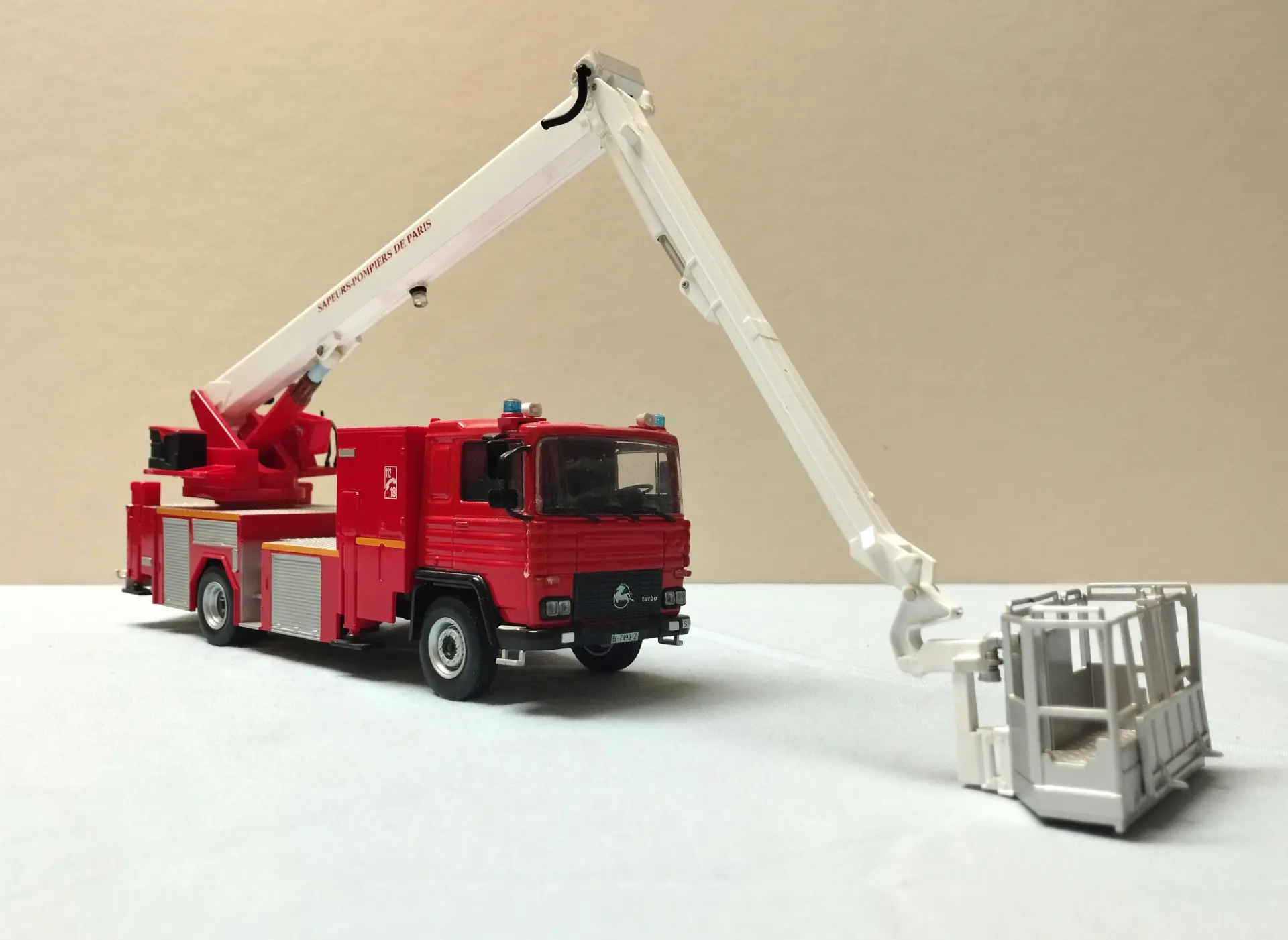 Camión de bomberos de color rojo con elevador hidráulico blanco extensible y cesta de rescate, perfecto para coleccionistas de camiones a escala 1:43 o entusiastas de las maquetas de camiones.