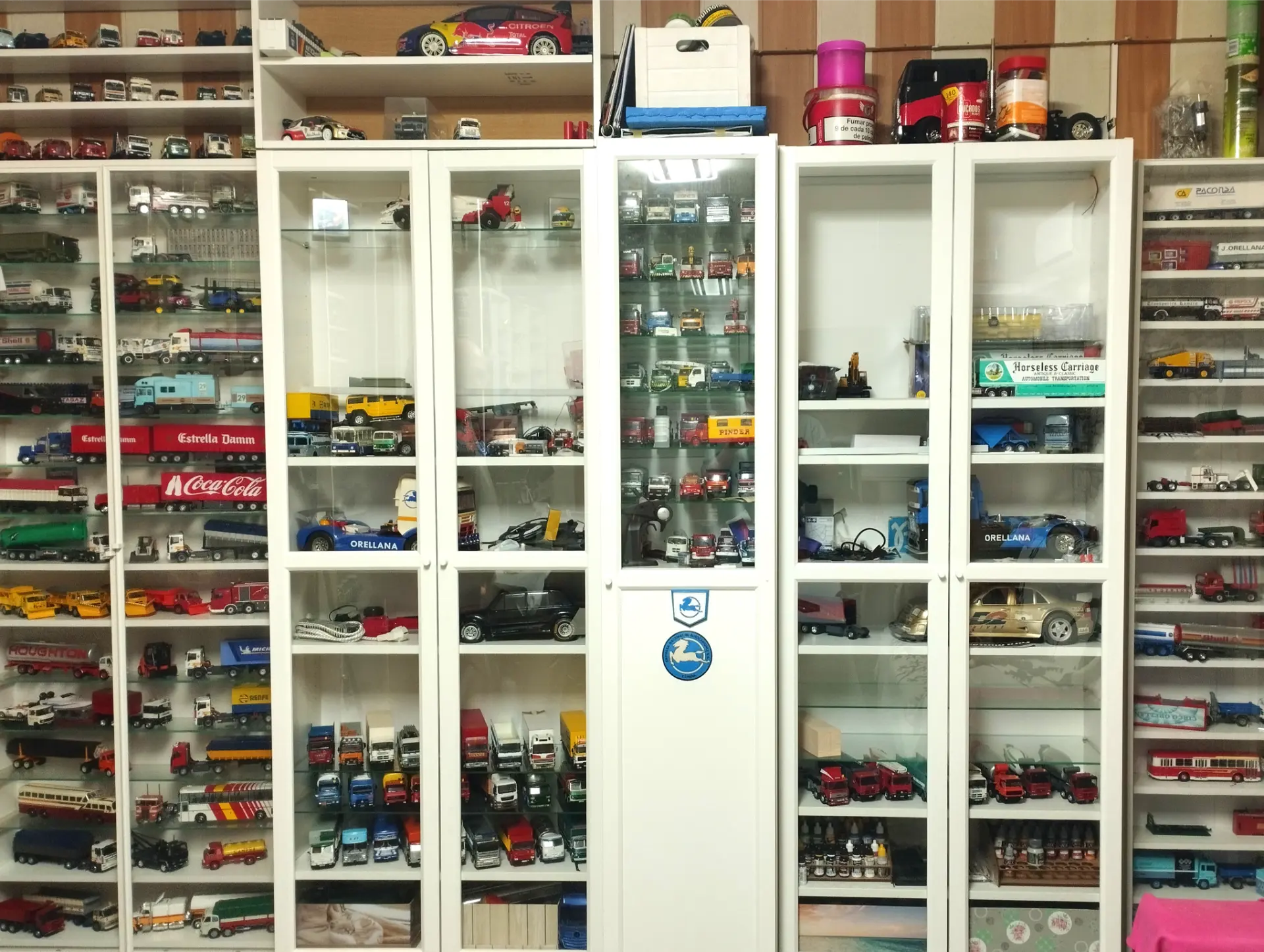 Vitrinas llenas de diversos modelos de coches, camiones y objetos de colección exhibidos en estantes, incluidas maquetas de camiones a escala 1/43 para los fanáticos del modelismo de camiones.