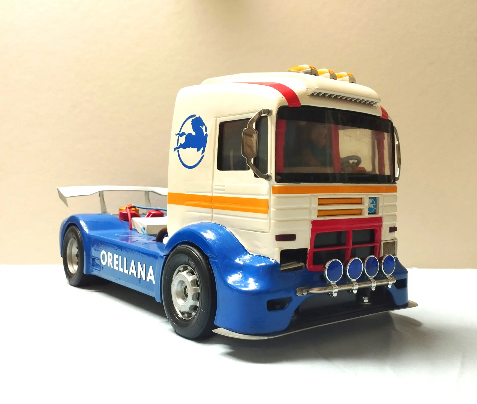 Un camión de carreras de juguete azul y blanco con "ORELLANA" en el costado, sobre un fondo liso, perfecto para coleccionistas de camiones a escala 1:43 o entusiastas de las maquetas de camiones.