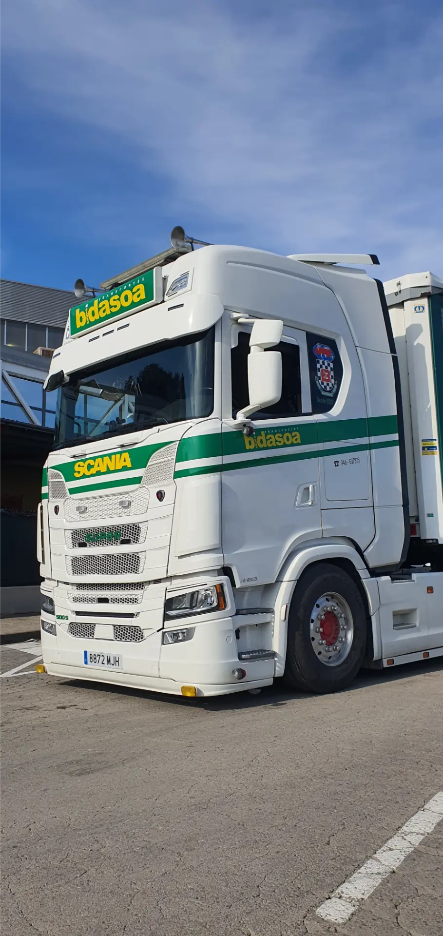 Camión Scania blanco con franjas verdes estacionado al aire libre en un día soleado, presentado por Solo Camión.