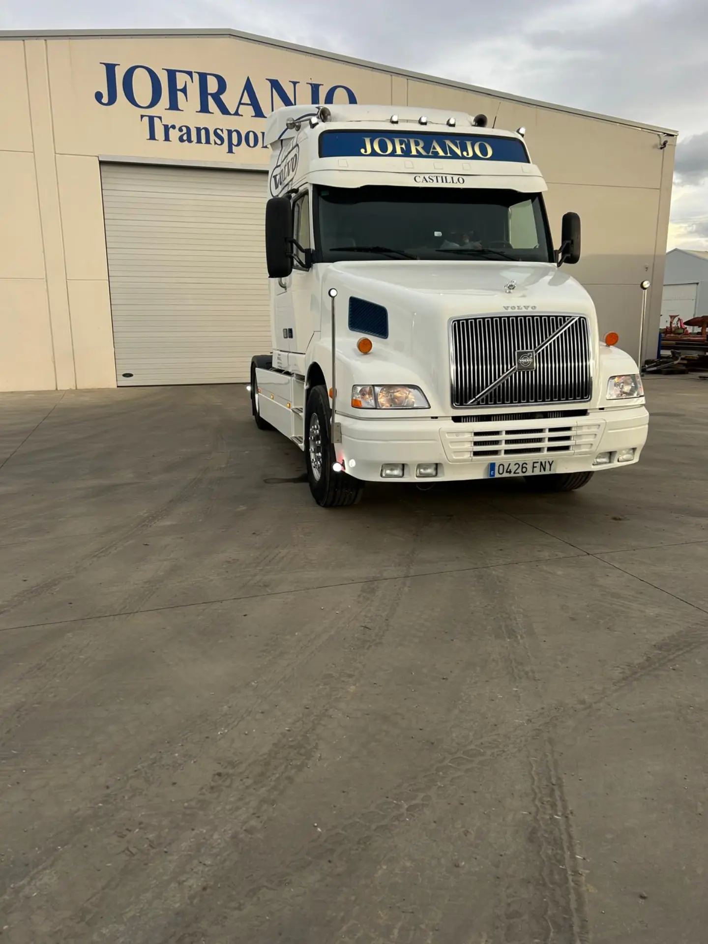 Camión Volvo blanco estacionado frente a un edificio con la etiqueta "JOFRANJO Transporte". Presentado en Solo Camión, este vehículo de JDC destaca por sus líneas limpias y su robusta presencia.