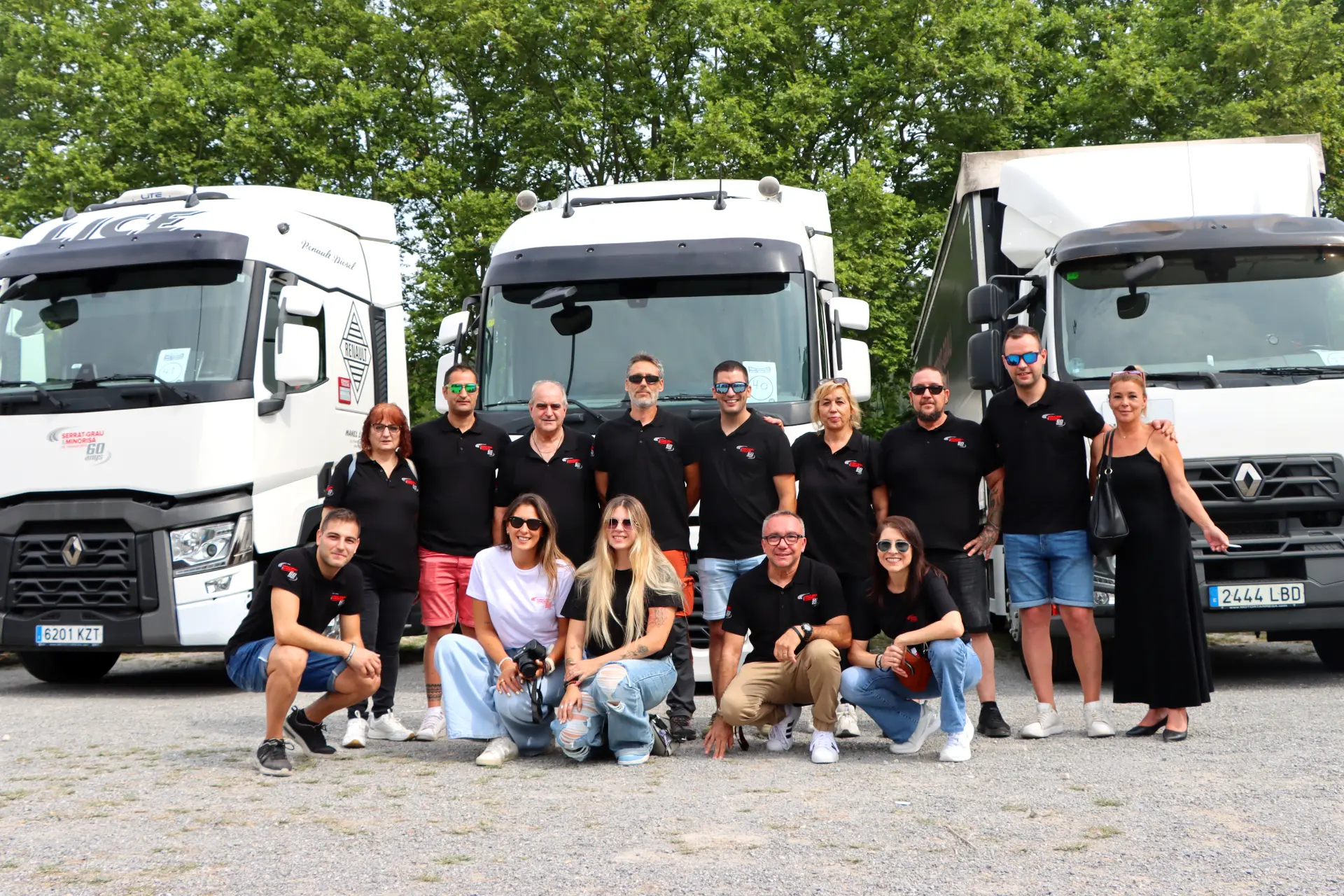 Un grupo de personas con camisas negras a juego posan al aire libre delante de tres grandes camiones blancos de Olot.