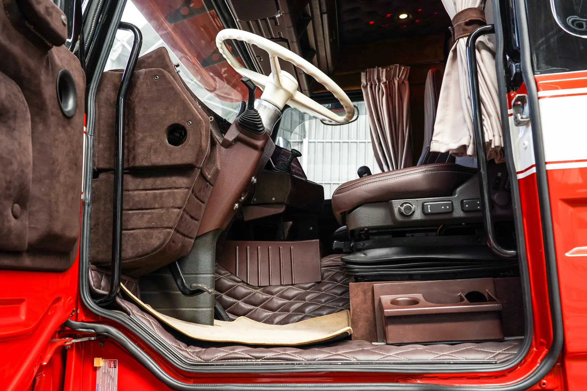 Interior de una cabina de camión roja con características de Borrador automático, mostrando el asiento del conductor, el volante y los mandos del salpicadero.