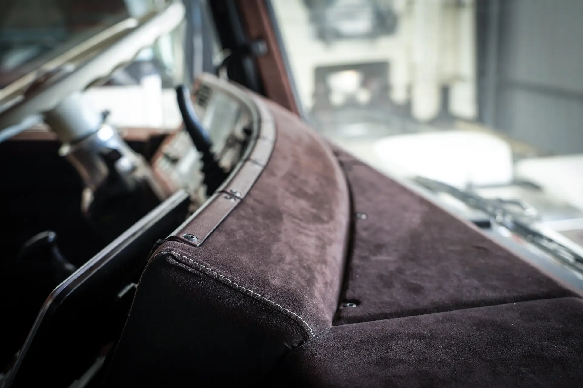Primer plano de un salpicadero de ante marrón en el interior de un coche de época, con la elegancia del diseño clásico y sutiles detalles de borrador automático, con elementos de fondo difuminados.
