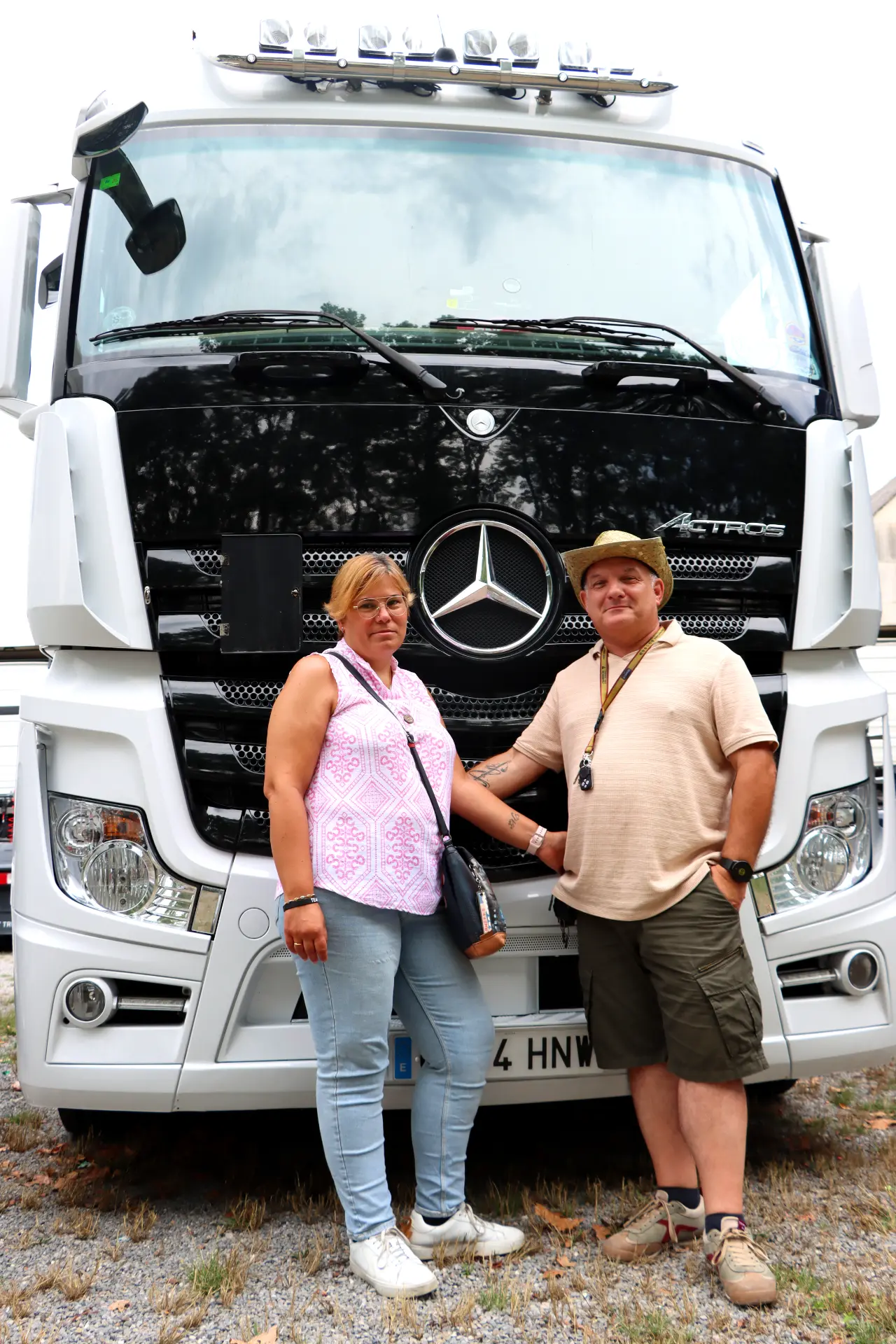 Dos personas permanecen de pie cogidas de la mano delante de un gran camión Mercedes-Benz blanco, mirando a la cámara, como dispuestas a emprender un viaje con su borrador automático.