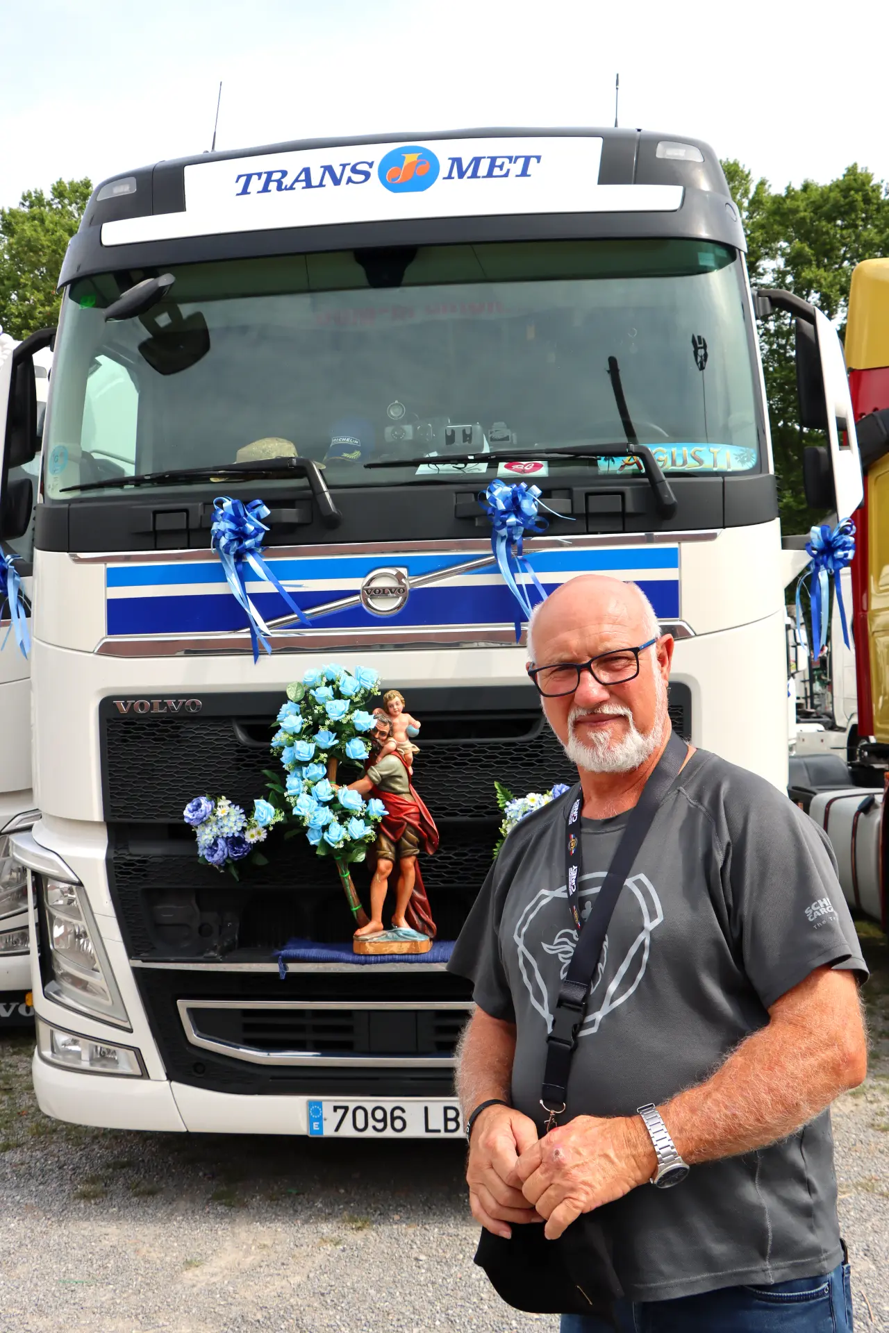 Un hombre delante de un camión decorado con lazos azules y la estatua de un santo en su parrilla en la Concentración de camiones de Olot.