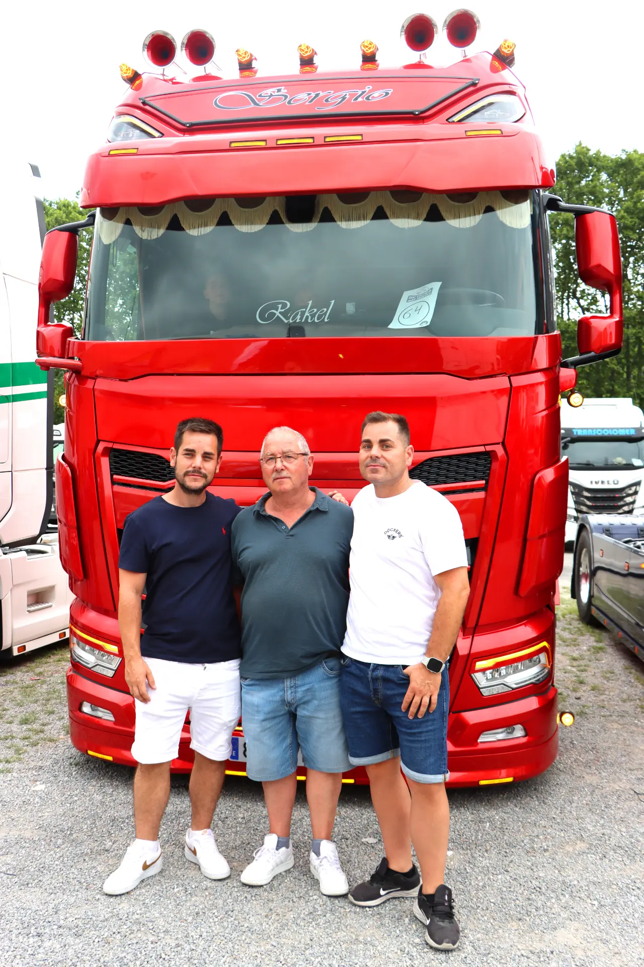 Tres hombres posan para una foto delante de un gran camión rojo en la concentración de camiones de Olot.
