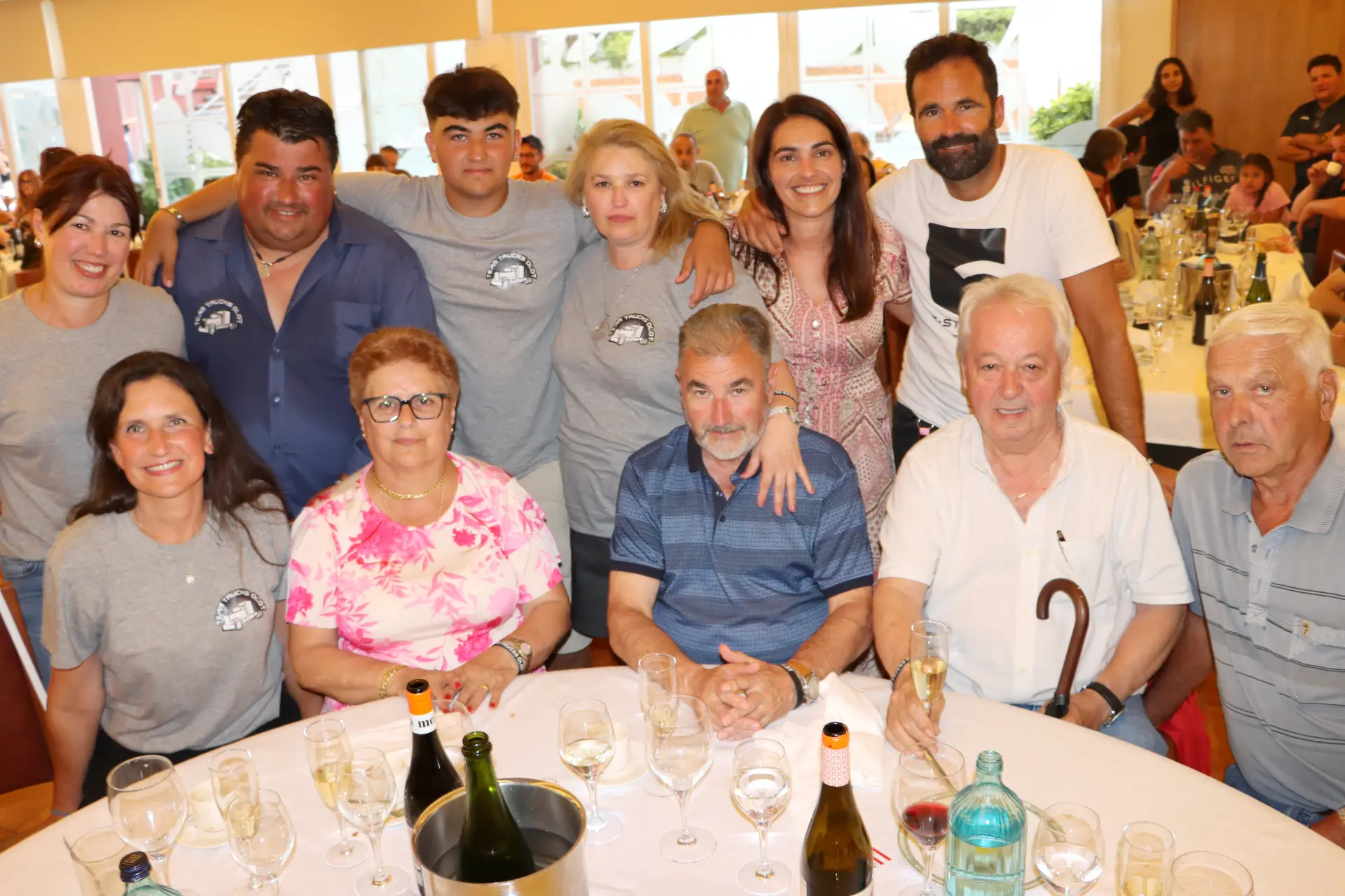 Un grupo de personas posa y sonríe alrededor de una mesa llena de vasos y botellas en una animada reunión en el interior de Olot, para celebrar después la concentración de camiones.