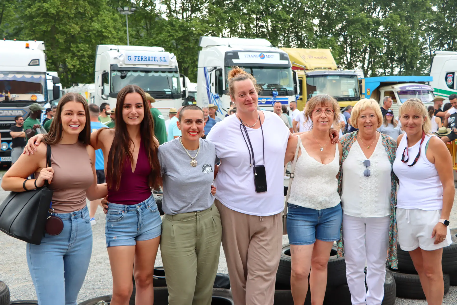 Siete mujeres sonríen juntas en un acto al aire libre en Olot, con camiones de la concentración de camiones y árboles al fondo.