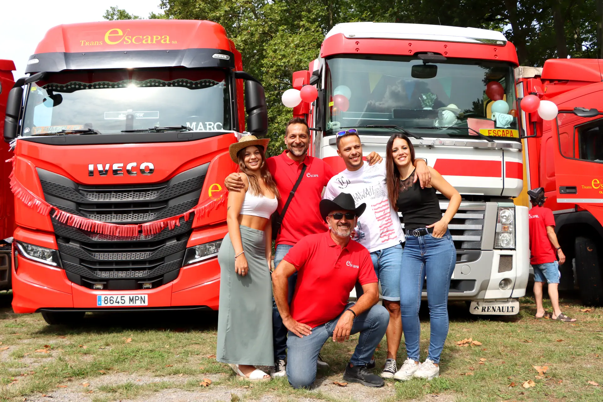 Cinco personas posan y sonríen delante de dos camiones rojos decorados en la XI Concentración de camiones de Olot al aire libre.